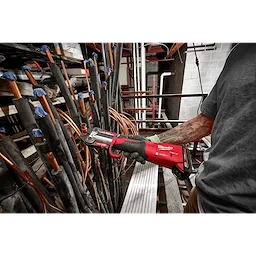 A person operates RLS ACR Press Jaws for M18 FORCE LOGIC Press Tools on a copper pipe in an industrial setting with various pipes.