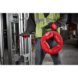 Construction worker uses 1/4" 100' Steel Fish Tape with a red case and black handle, wearing safety gear on a job site.