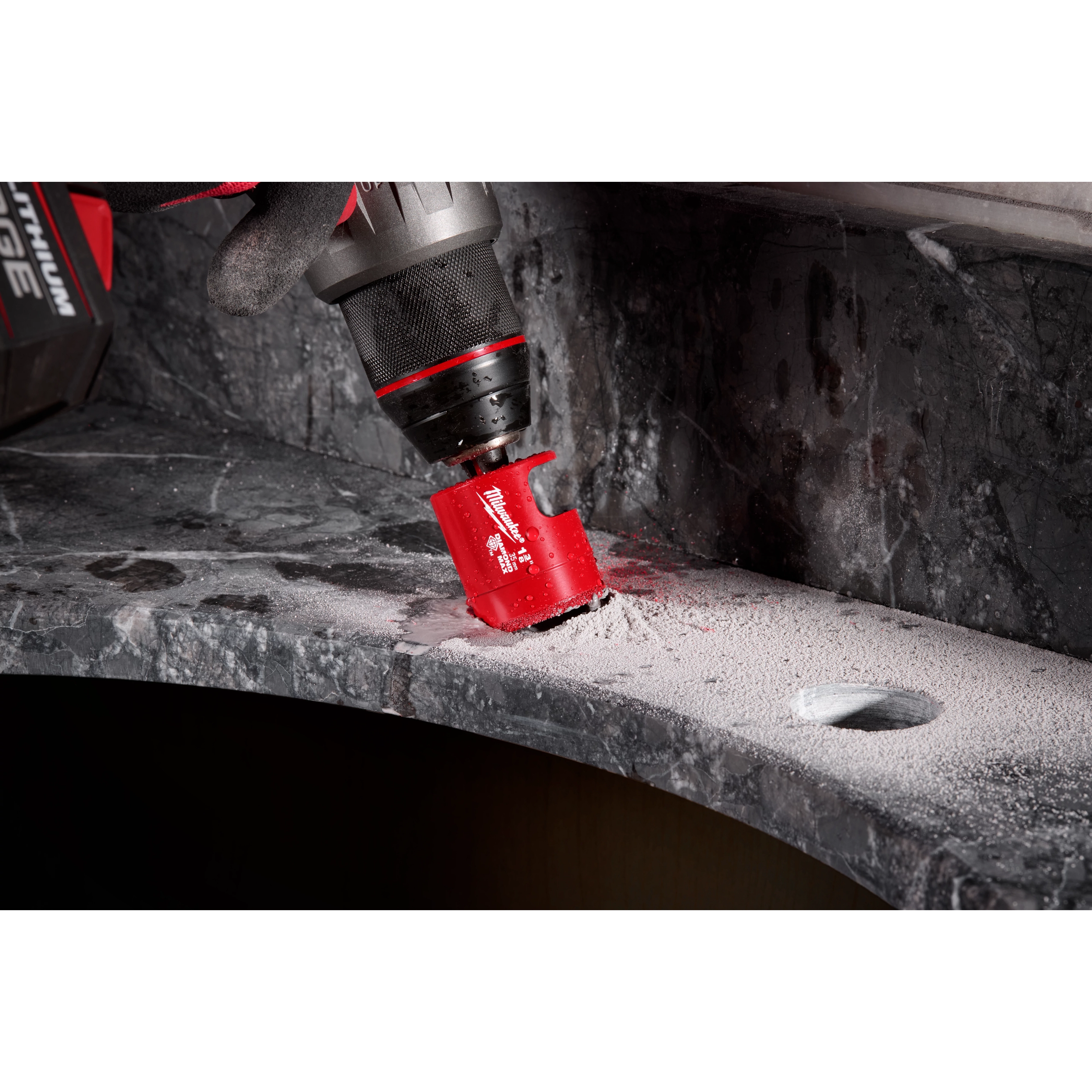 A Milwaukee® 1-3/8" DIAMOND MAX™ Hole Saw Bit attached to a drill is cutting into a grey stone surface, creating a hole. Dust and debris are visible around the drilling area.