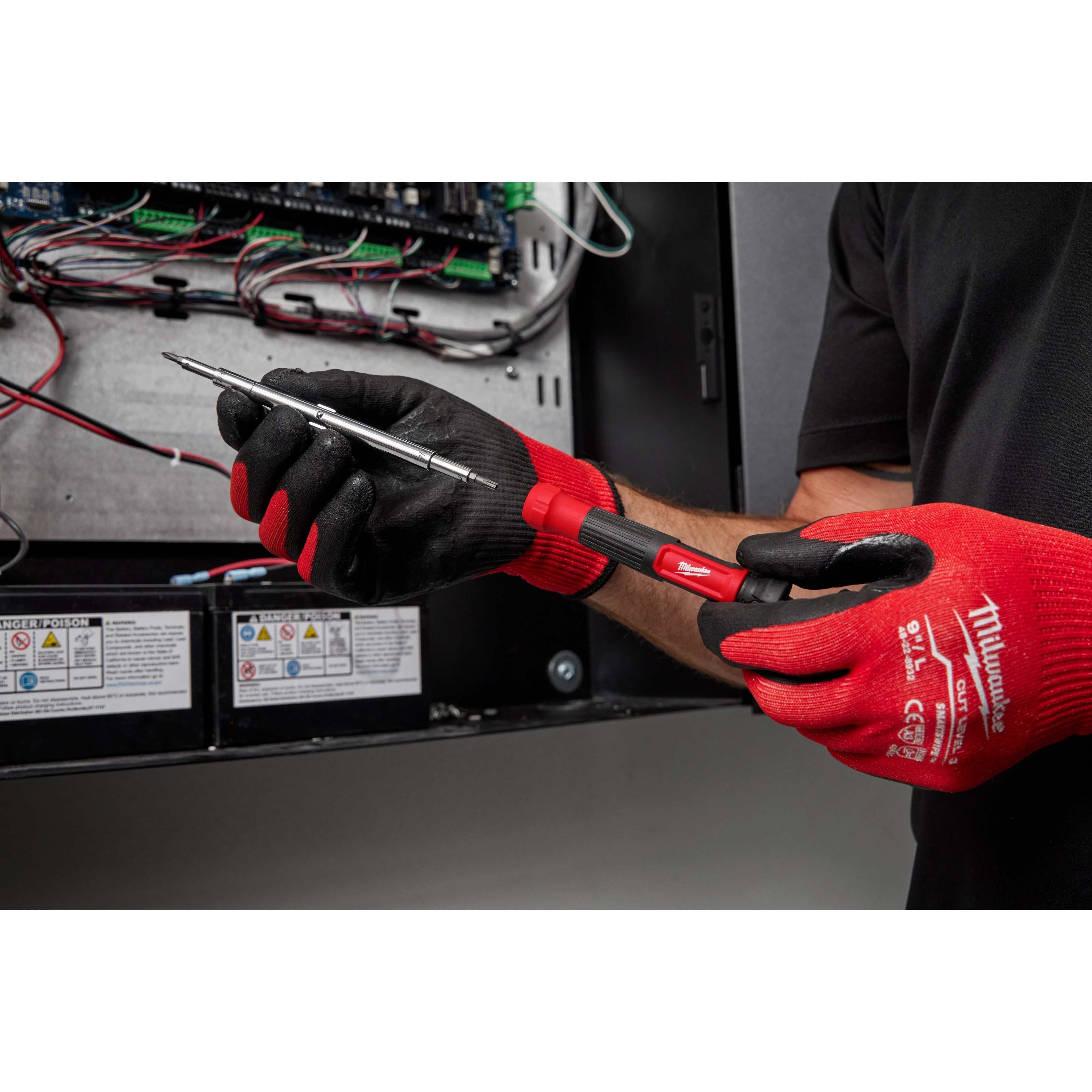 Person wearing red and black gloves using a 14-in-1 Precision Multi-Bit Screwdriver to work on an electrical panel.