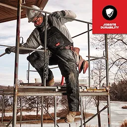 Worker wearing FREEFLEX Insulated Bib Overalls, standing on scaffolding at a construction site. Red badge reads "Jobsite Durability."