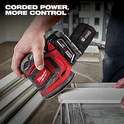 A person is using a red Milwaukee sander from the M18 5 Tool Combo Kit on a piece of wood trim. The sander features a black dust bag attached at the back. The text "Corded Power, More Control" appears in the upper left corner of the image.