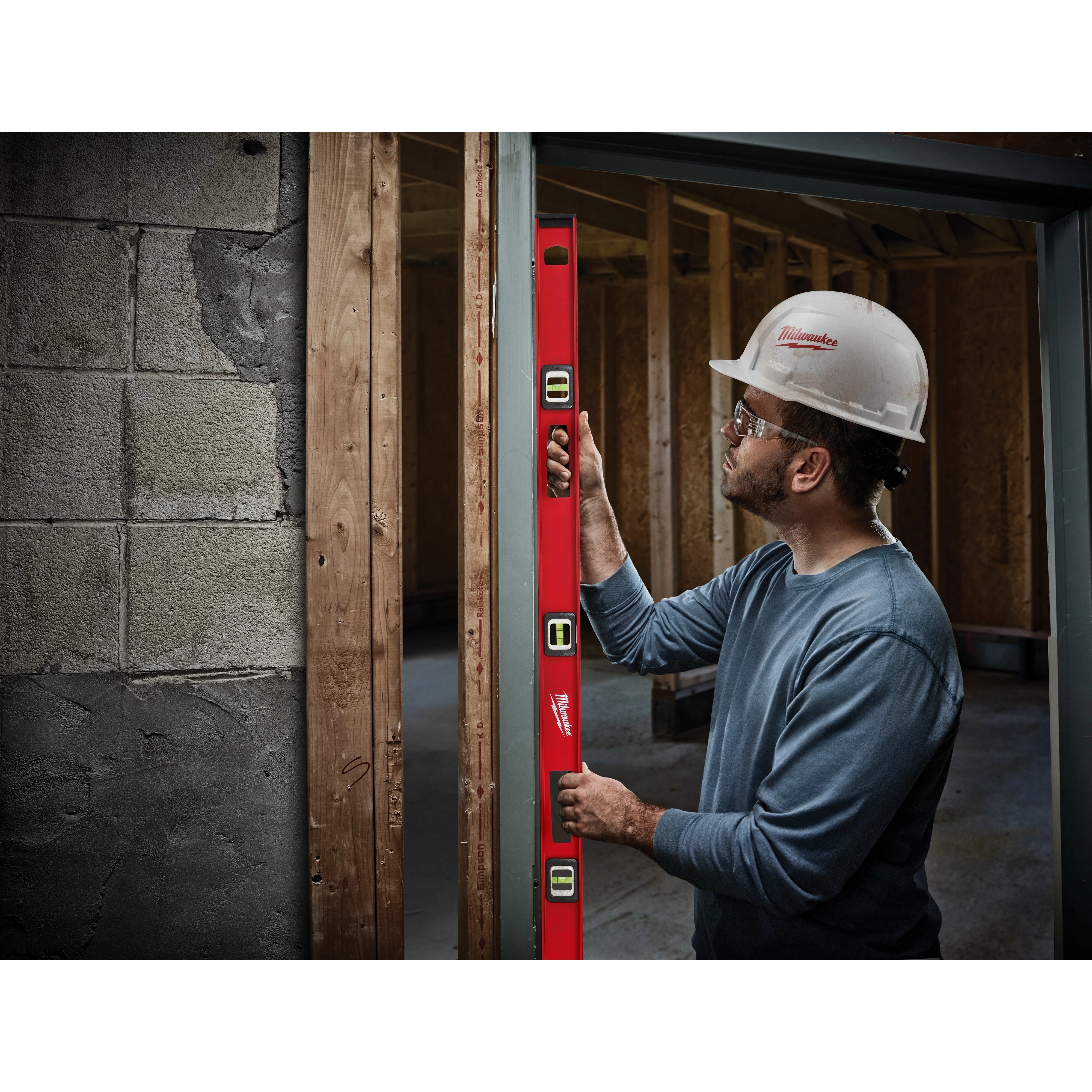 A construction worker uses a Milwaukee 48" Magnetic I-Beam Level to ensure vertical alignment of a door frame in a building under construction.