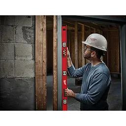 A construction worker uses a Milwaukee 48" Magnetic I-Beam Level to ensure vertical alignment of a door frame in a building under construction.