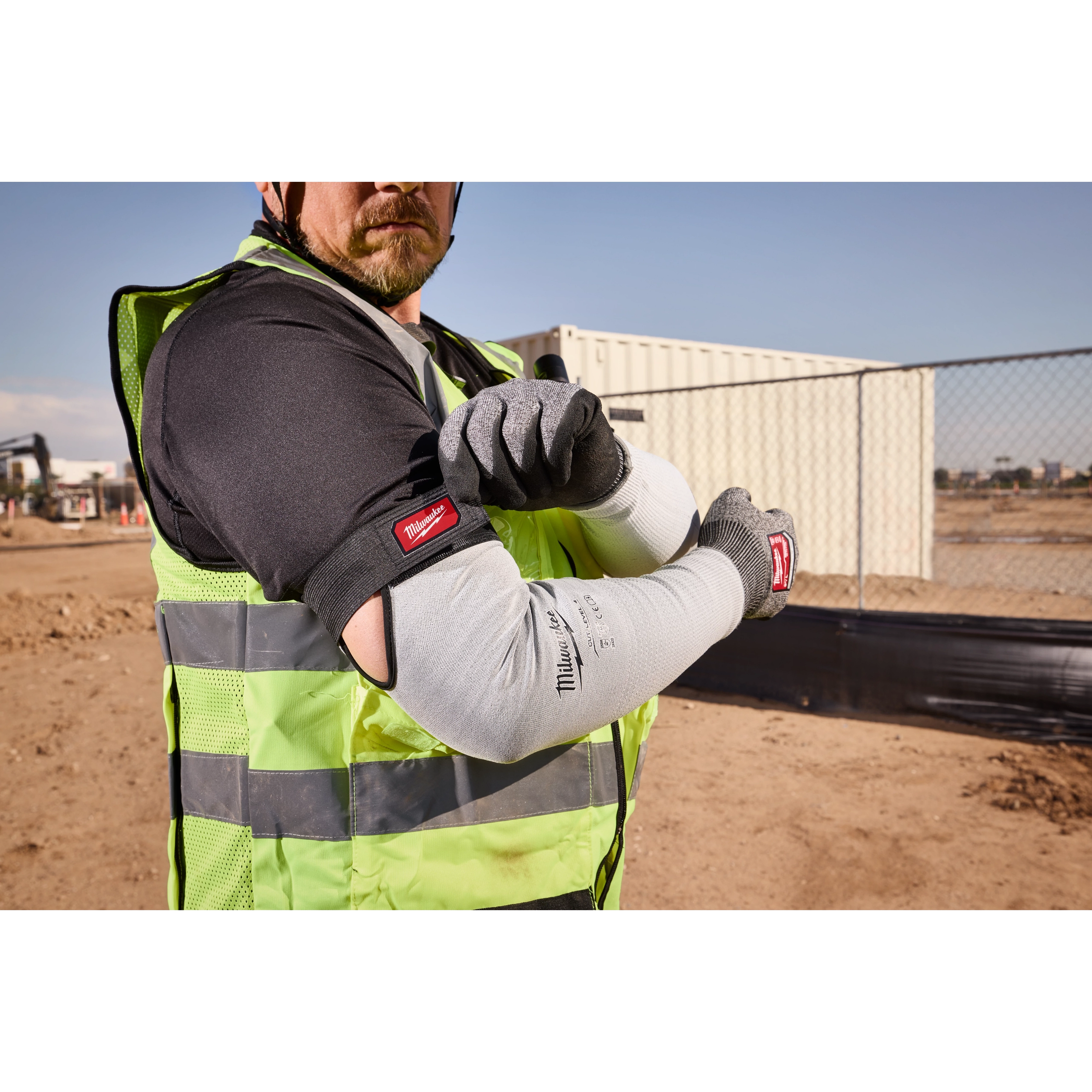 Worker wearing Cut Level 4 Protective Sleeves on a construction site, with a high-visibility vest and gloves.