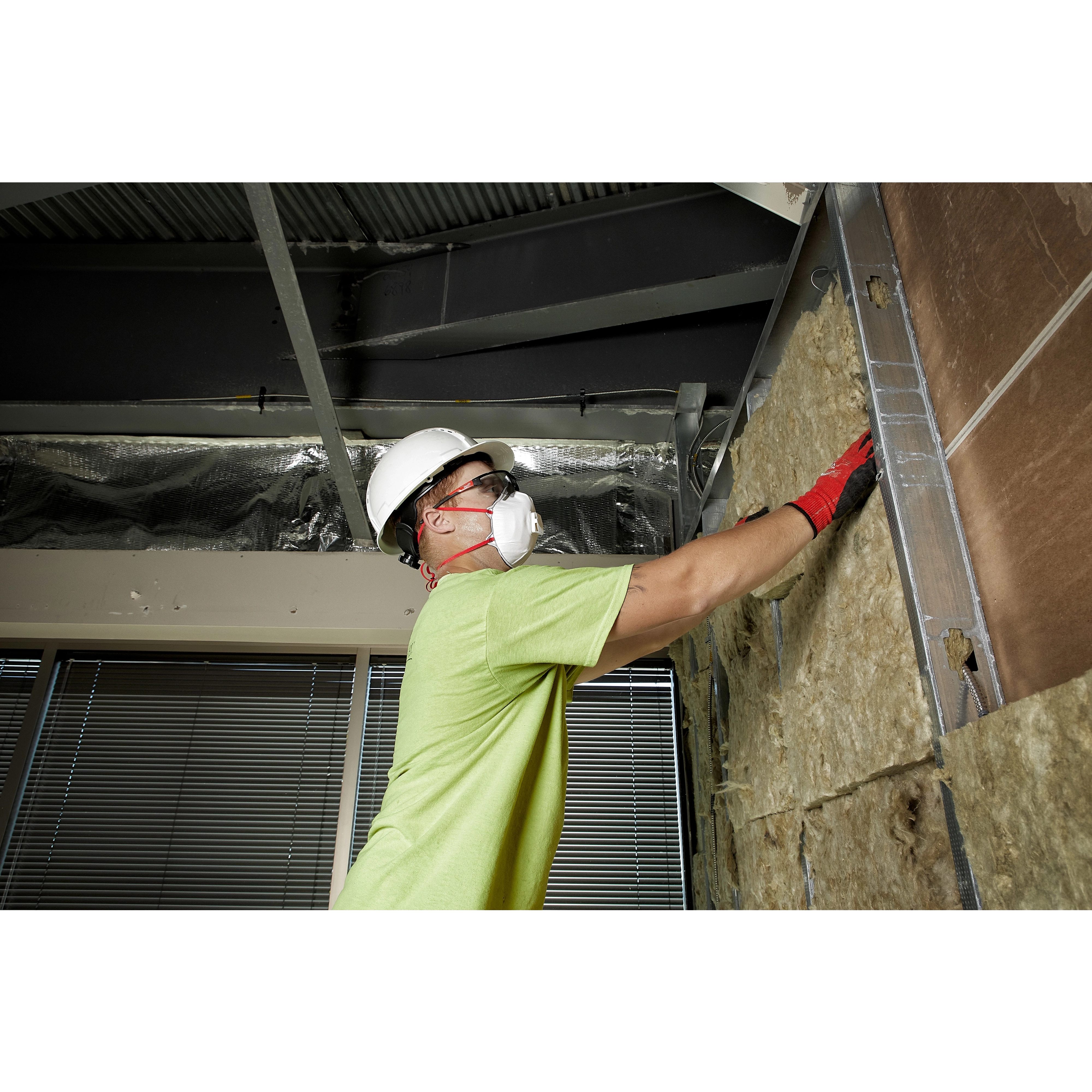 Worker wearing Safety Glasses - Gray Fog-Free Lenses, a hard hat, and mask installing insulation in a construction setting.