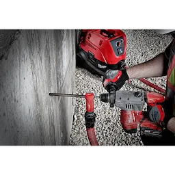 SDS%20Vacuum%20Bit in use with a power drill, drilling into a concrete wall, connected to a red vacuum system on gravel ground.