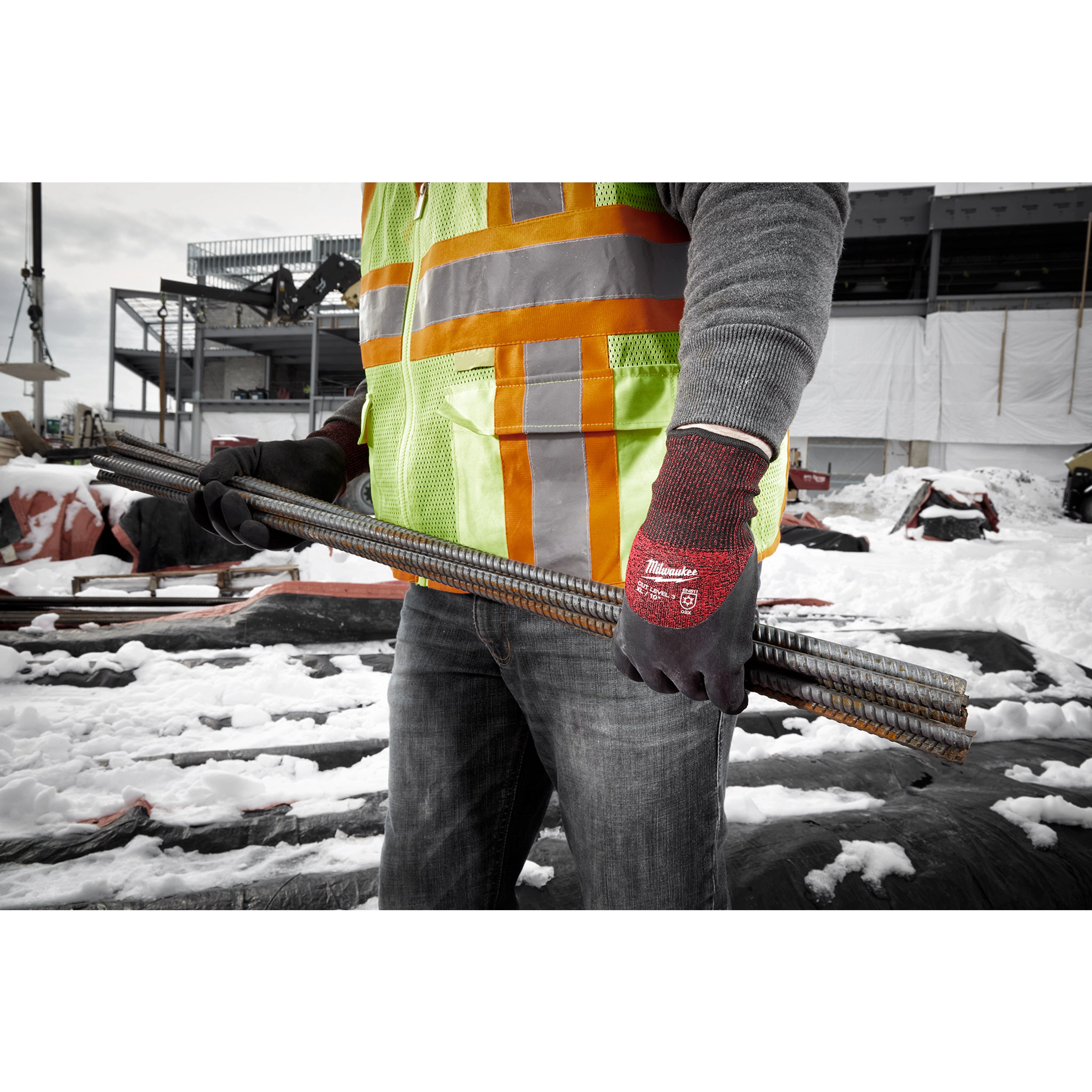 Worker wearing Cut Level 3 Winter Insulated Gloves - XL holds metal rebar at a construction site, dressed in a safety vest.