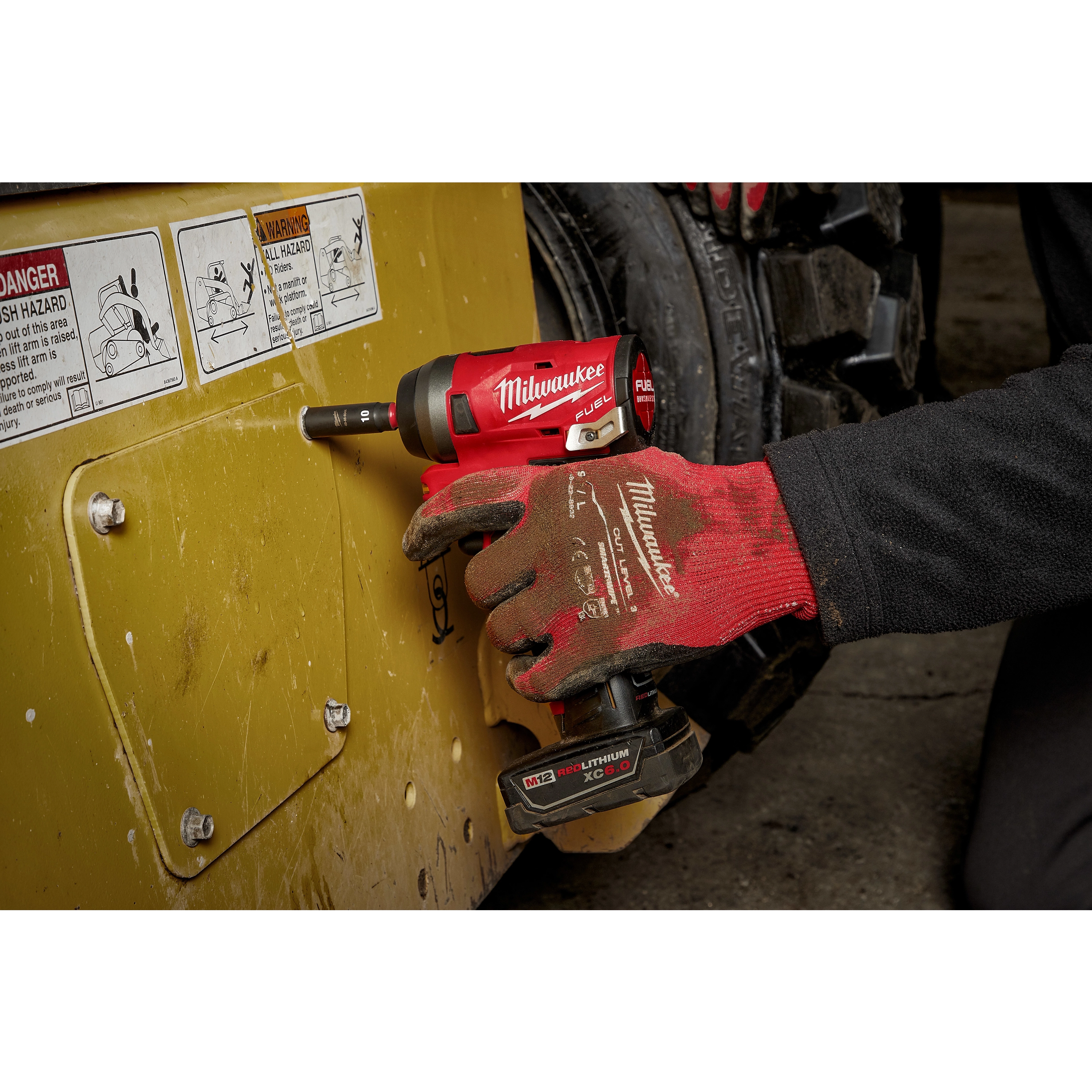 Gloved hand uses a red and black Milwaukee power tool equipped with SHOCKWAVE Impact Duty 1/4" Drive 14MM Deep 6 Point Socket to tighten a bolt.