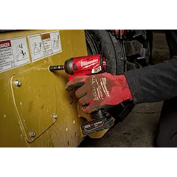 Gloved hand uses a red and black Milwaukee power tool equipped with SHOCKWAVE Impact Duty 1/4" Drive 14MM Deep 6 Point Socket to tighten a bolt.