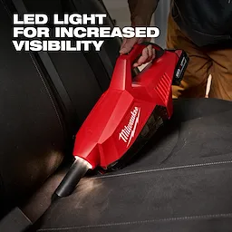 Person using the M18 Brushless Handheld Vacuum with an LED light to clean a car seat, enhancing visibility for thorough cleaning.