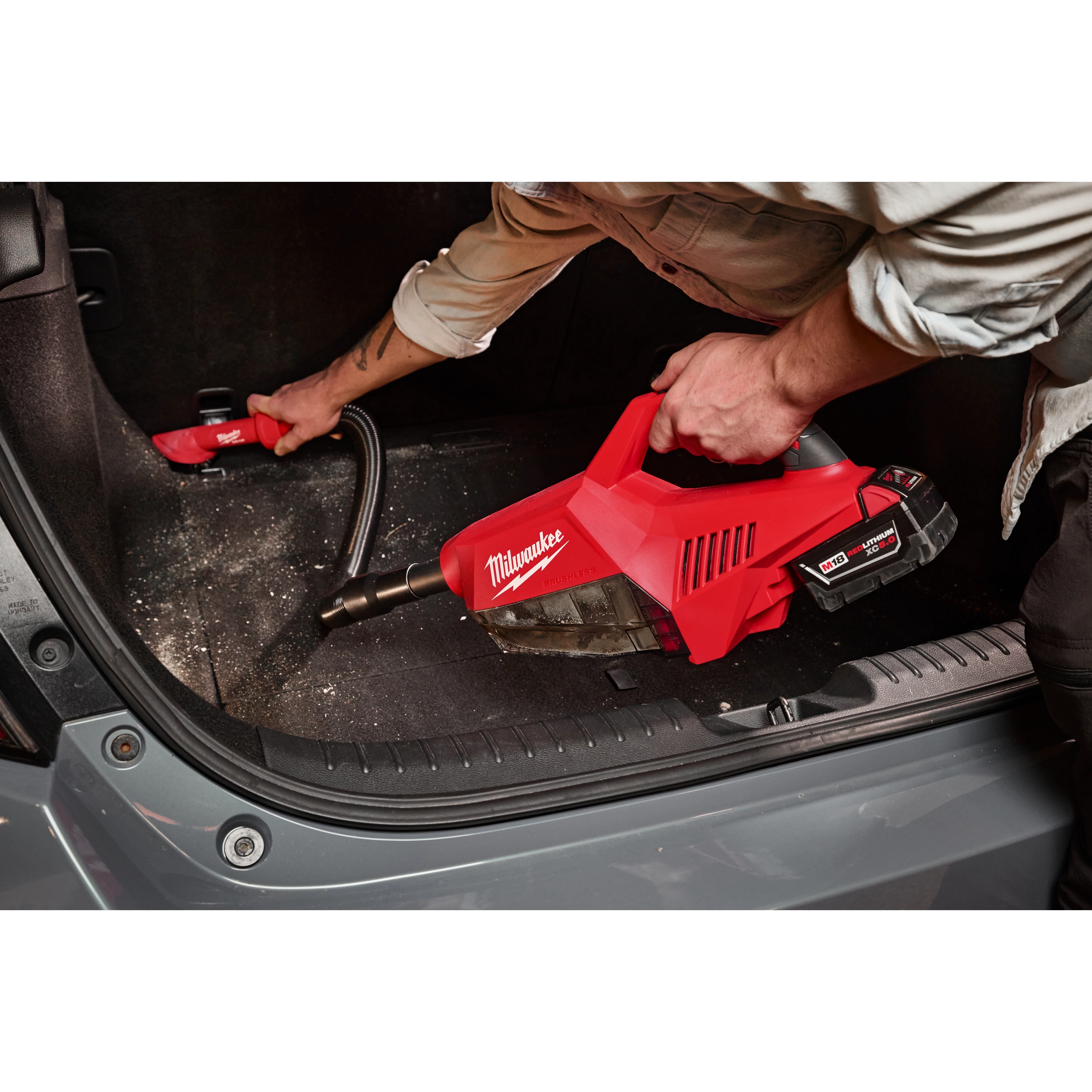 A person uses the M18 Brushless Handheld Vacuum to clean the trunk of a car.