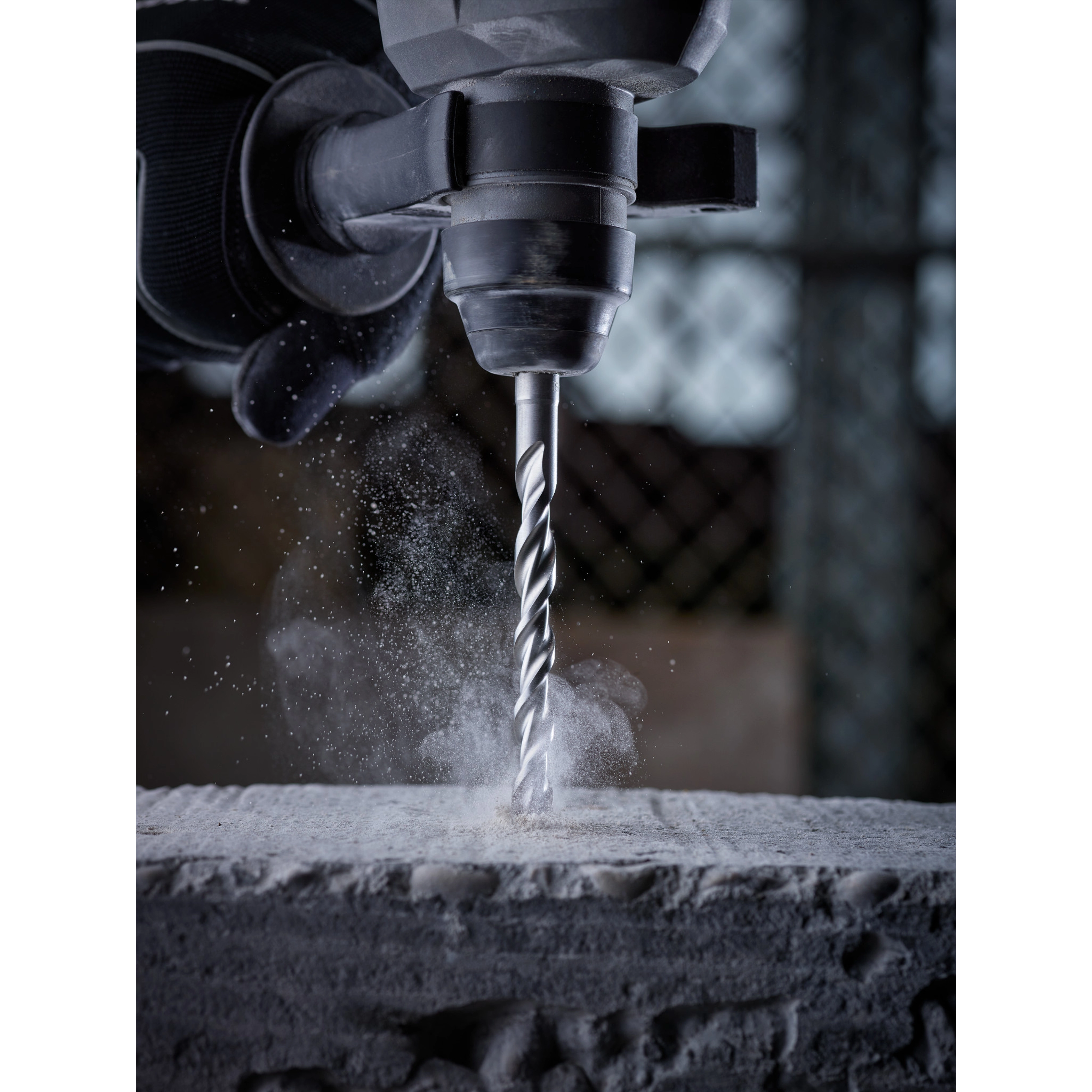 SDS Plus M2 2-Cutter Drill Bits in action, drilling into concrete with dust particles around the bit, attached to a power drill.