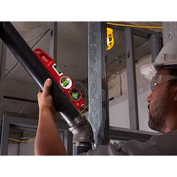 A person installs a pipe using a Block Torpedo Level in a construction setting. The level is red with two green bubble vials.
