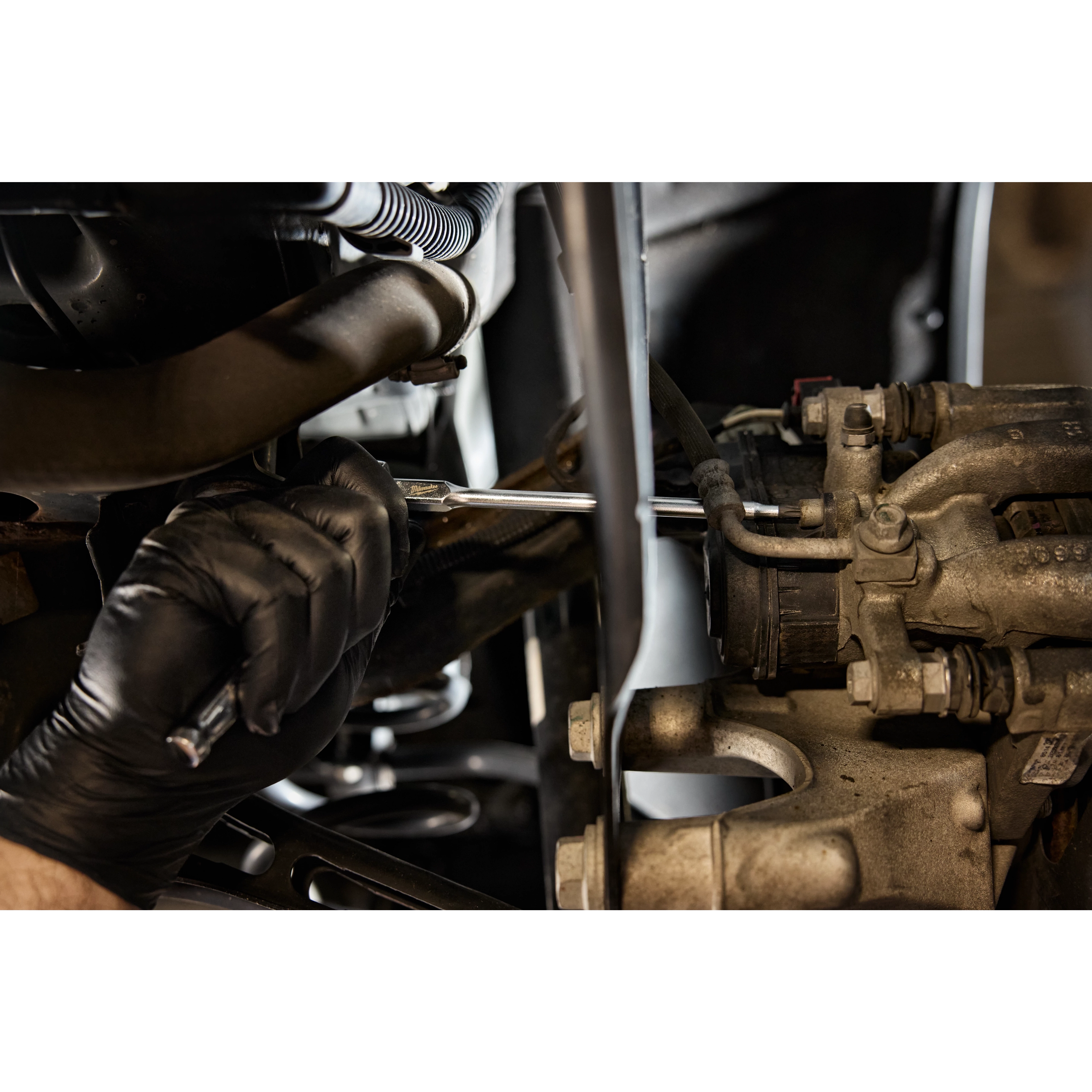 A mechanic's hand in a black glove uses a 1/4" Drive T27 Long TORX Bit Socket to work on an engine component inside a vehicle.