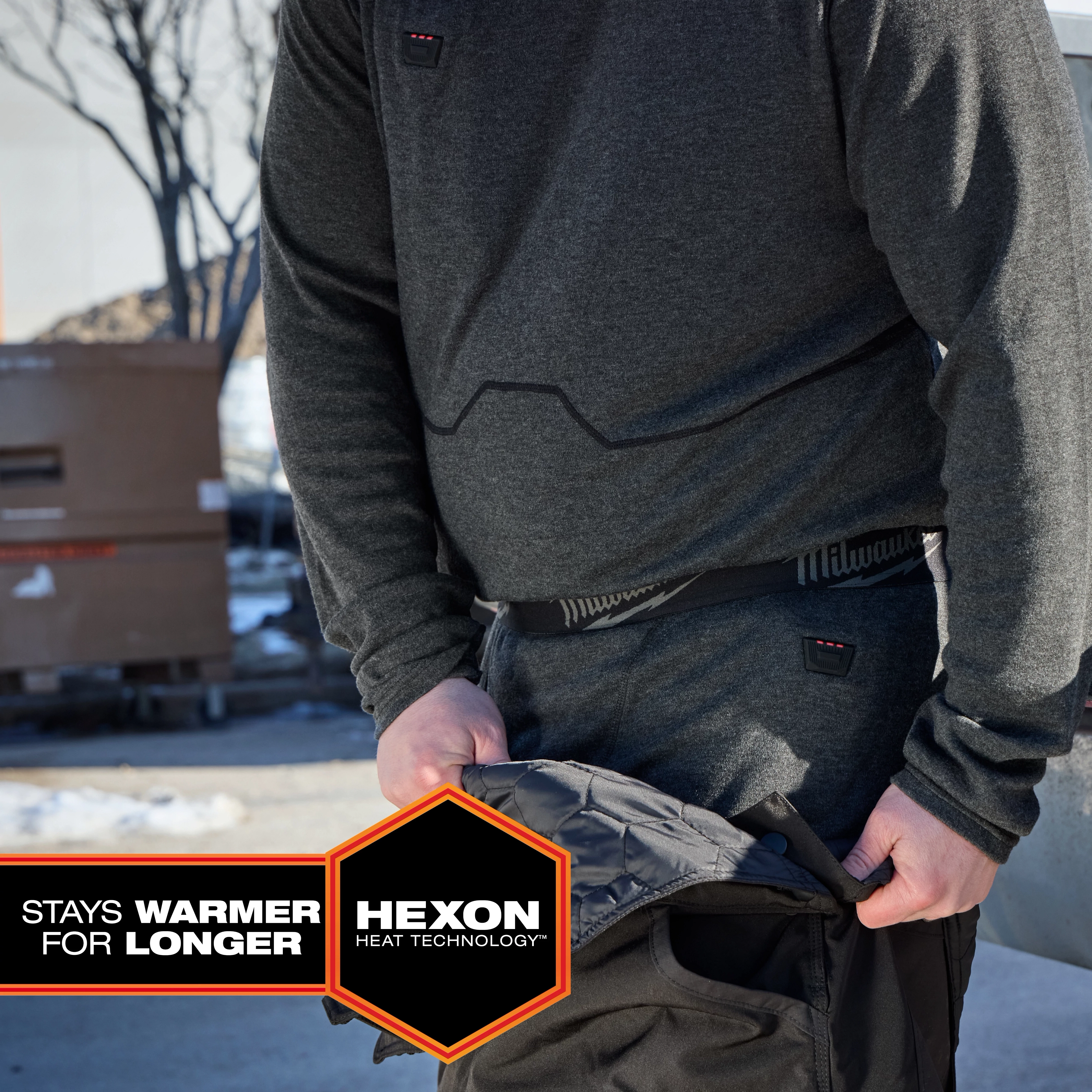 Person wearing Milwaukee Heated Merino Wool Baselayer Pants outdoors, adjusting outer pants in a snowy setting.