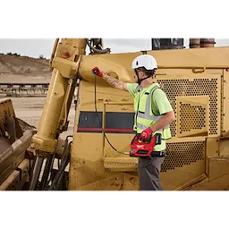 Worker using an M18 FUEL Grease Gun to service a large construction vehicle outdoors.