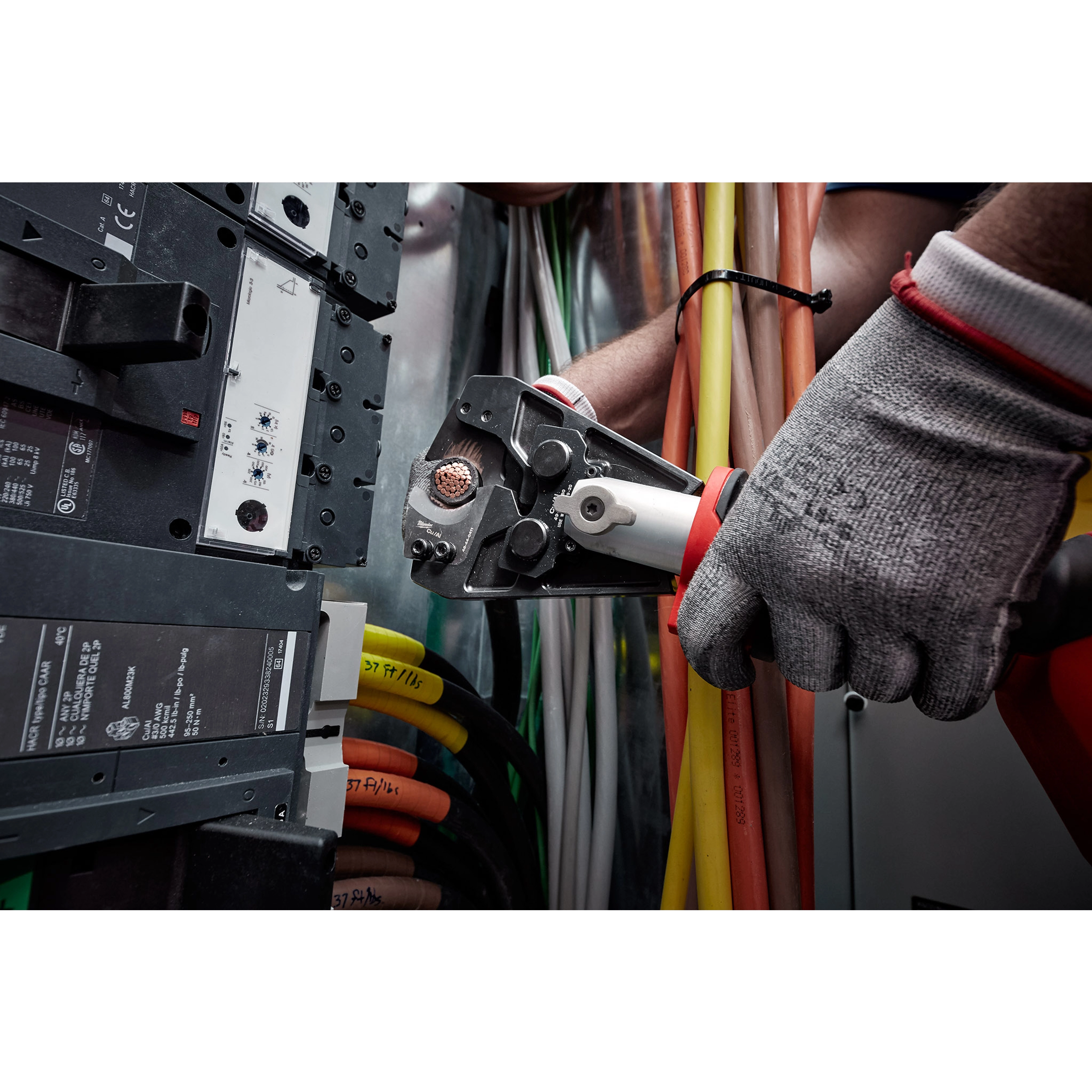 A gloved hand operates a 750 MCM Cu/Al Cutting Jaw, cutting through electrical cables in an industrial setting.