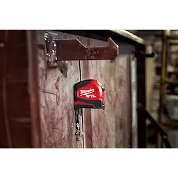 Red and black 10ft/3 Keychain Tape Measure with LED attached to a metallic surface using its magnetic back, keys hanging below.