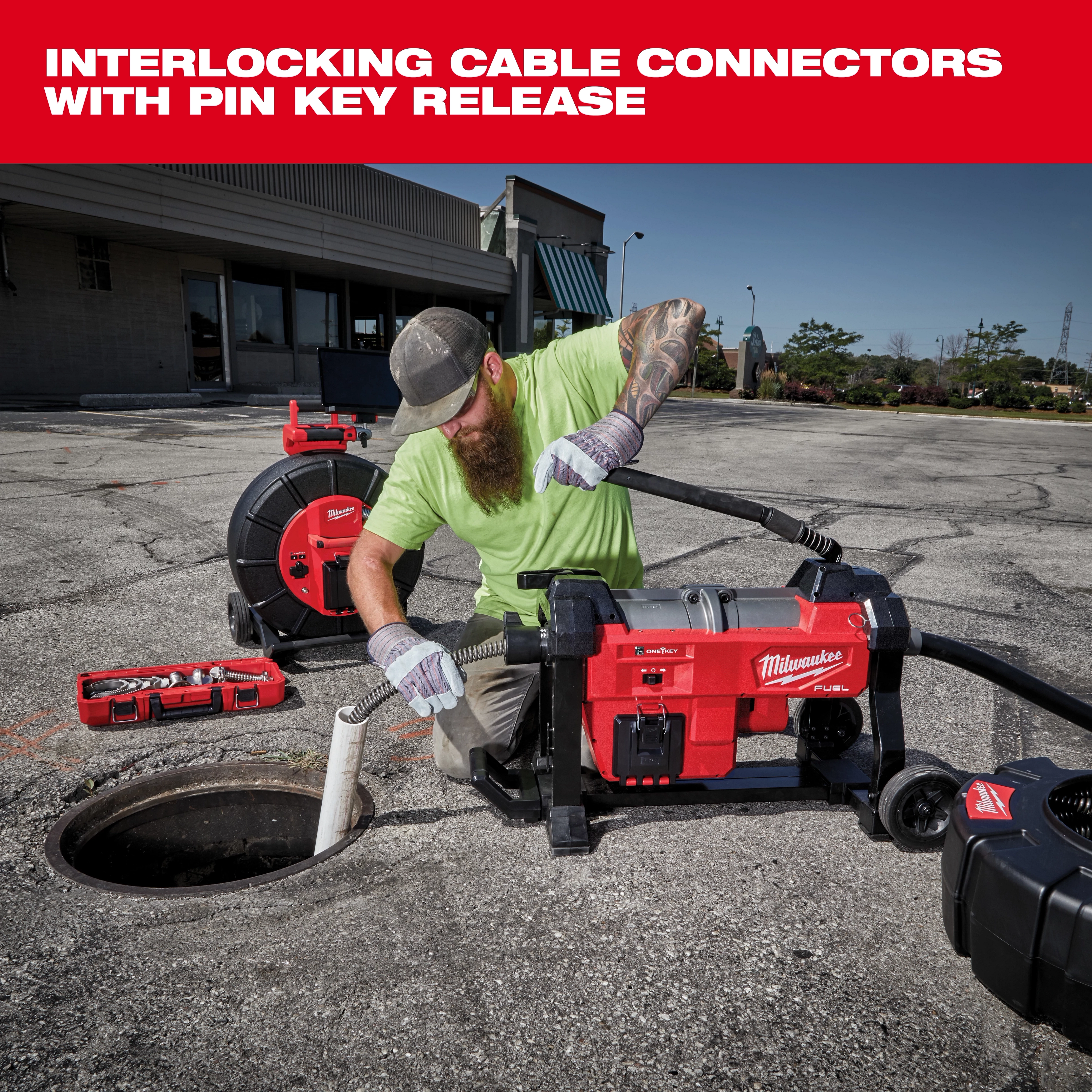 Person using Milwaukee interlocking cable connectors with pin key release system to insert a drainage tool into a large outdoor drainage pipe. Various Milwaukee tools and equipment are arranged nearby on the ground, including handheld tools and a portable reel.