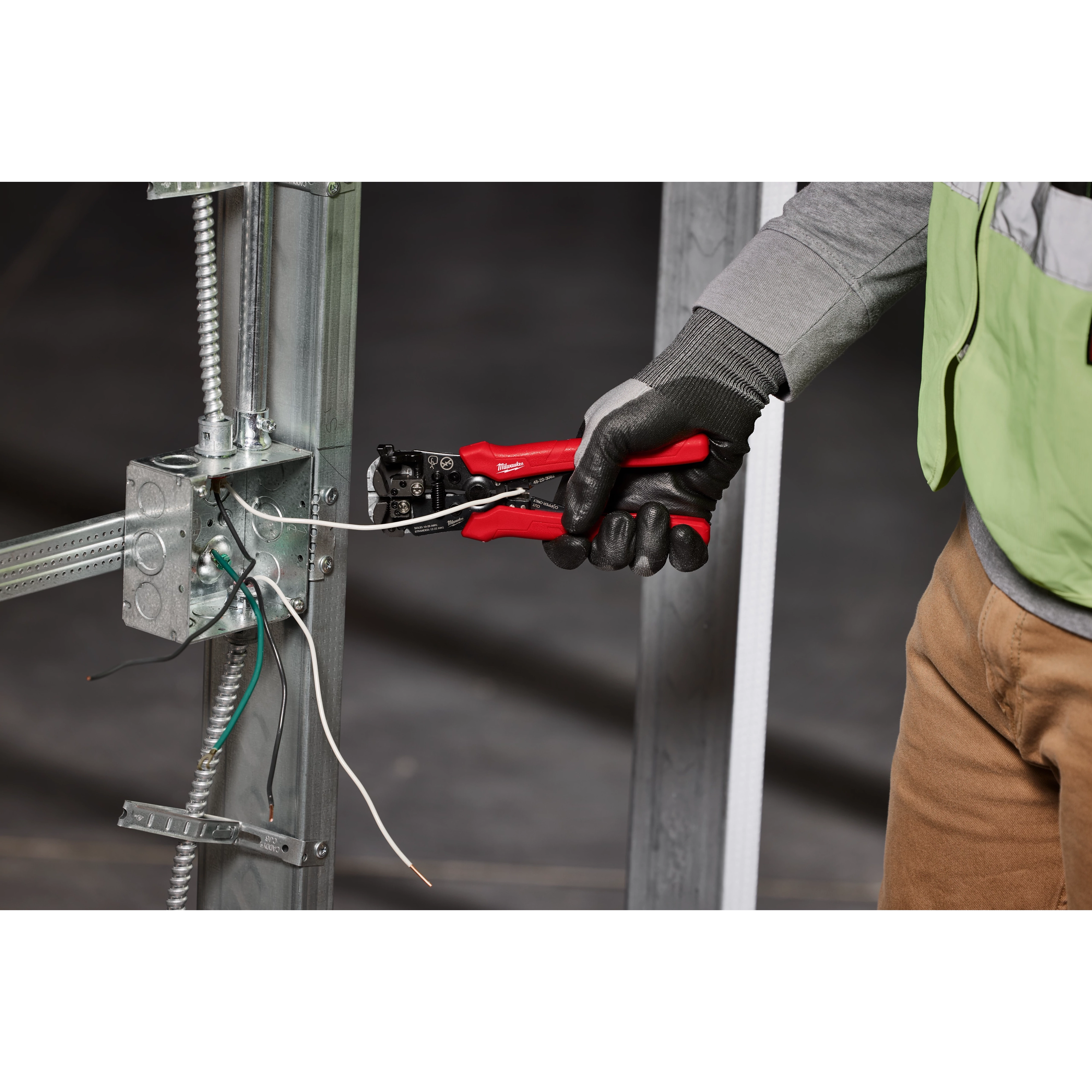 A person wearing gloves is using a Self-Adjusting Wire Stripper & Cutter to strip wires attached to a metal frame.