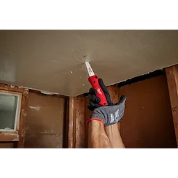 A person in gloves uses a Folding Jab Saw to cut a marked circle in a ceiling during a renovation project.