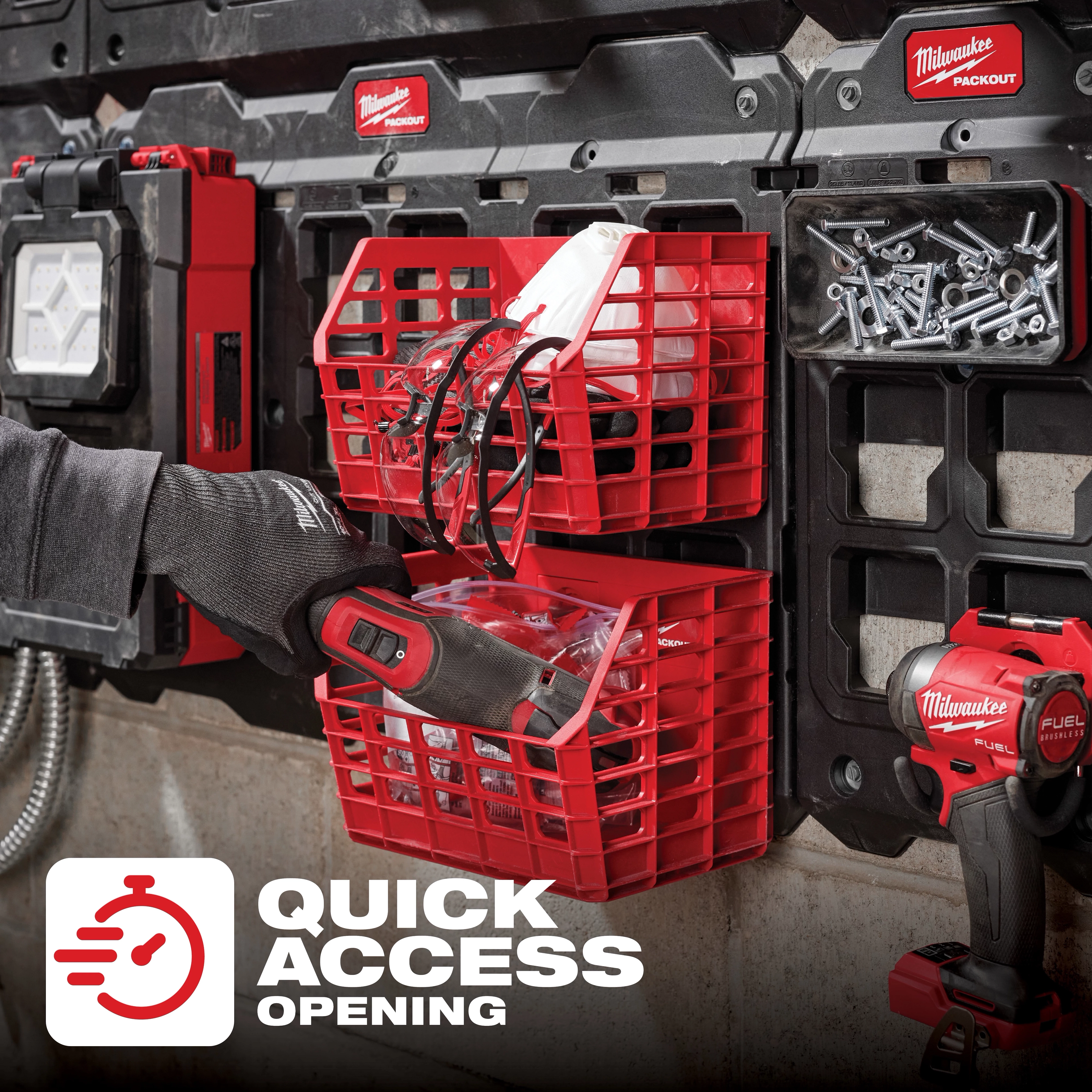 PACKOUT Compact Wall Basket mounted on a wall grid holds various tools and accessories. A hand is placing a tool into the lower basket.