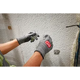 Person wearing Cut Level 3 High-Dexterity Nitrile Dipped Gloves - XL, handling a metal object against a textured wall.