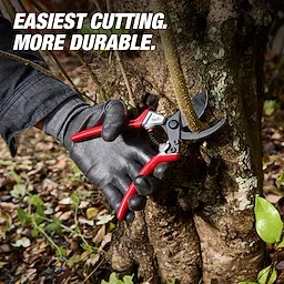 A gloved hand uses a 1" Pruner with red handles to cut a branch against a tree trunk. The image features the text "EASIEST CUTTING. MORE DURABLE." surrounded by leaves and outdoor ground cover.