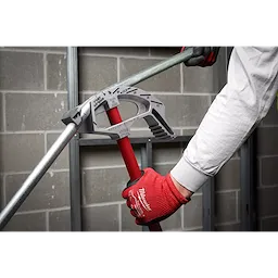 A person wearing a white shirt and red gloves uses Offset Jobsite Scissors to cut a metal pipe against a concrete block wall background.