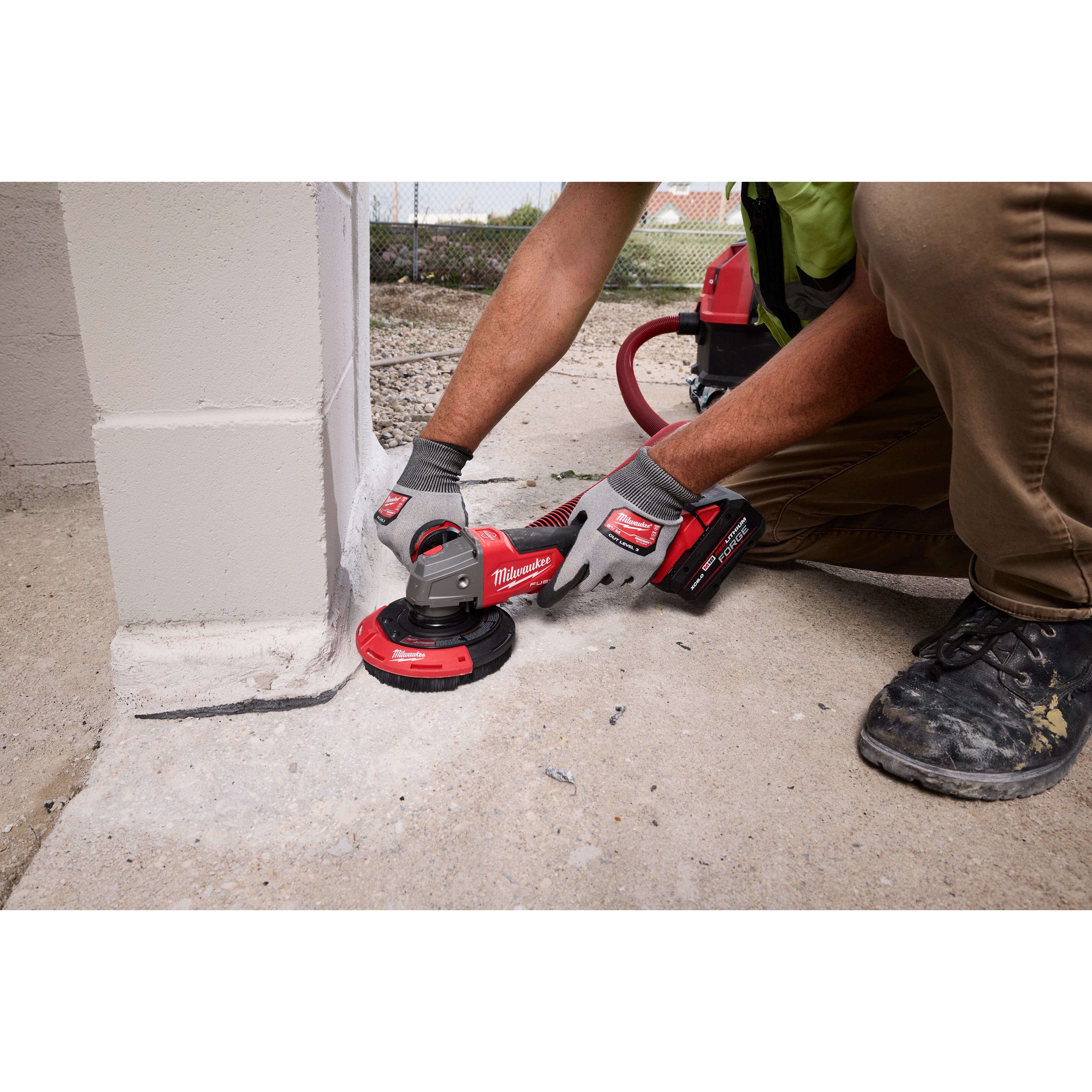 A worker uses the Milwaukee 4-1/2" - 5" Surface Grinding Dust Shroud on a surface. The tool is connected to a vacuum system for dust collection, ensuring cleaner work while grinding concrete.