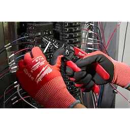A technician uses the 8-20 AWG Dipped Grip Wire Stripper & Cutter (USA) to strip a wire in an electrical panel. The tool features dipped grips for comfort and multiple cutting and stripping holes. The technician wears red and black gloves while working with the wires.