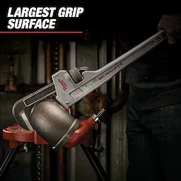Milwaukee pipe wrench gripping a large metal pipe with the text "Largest Grip Surface" at the top left. The wrench is silver with a red Milwaukee logo and is being used by a person wearing dark clothing.