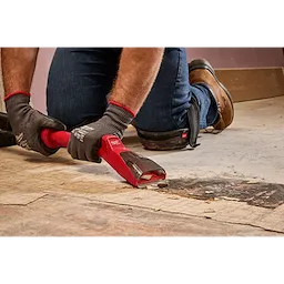 Person using the AIR-TIP Debris Scraper to remove debris from a floor while wearing work gloves, jeans, and brown boots.