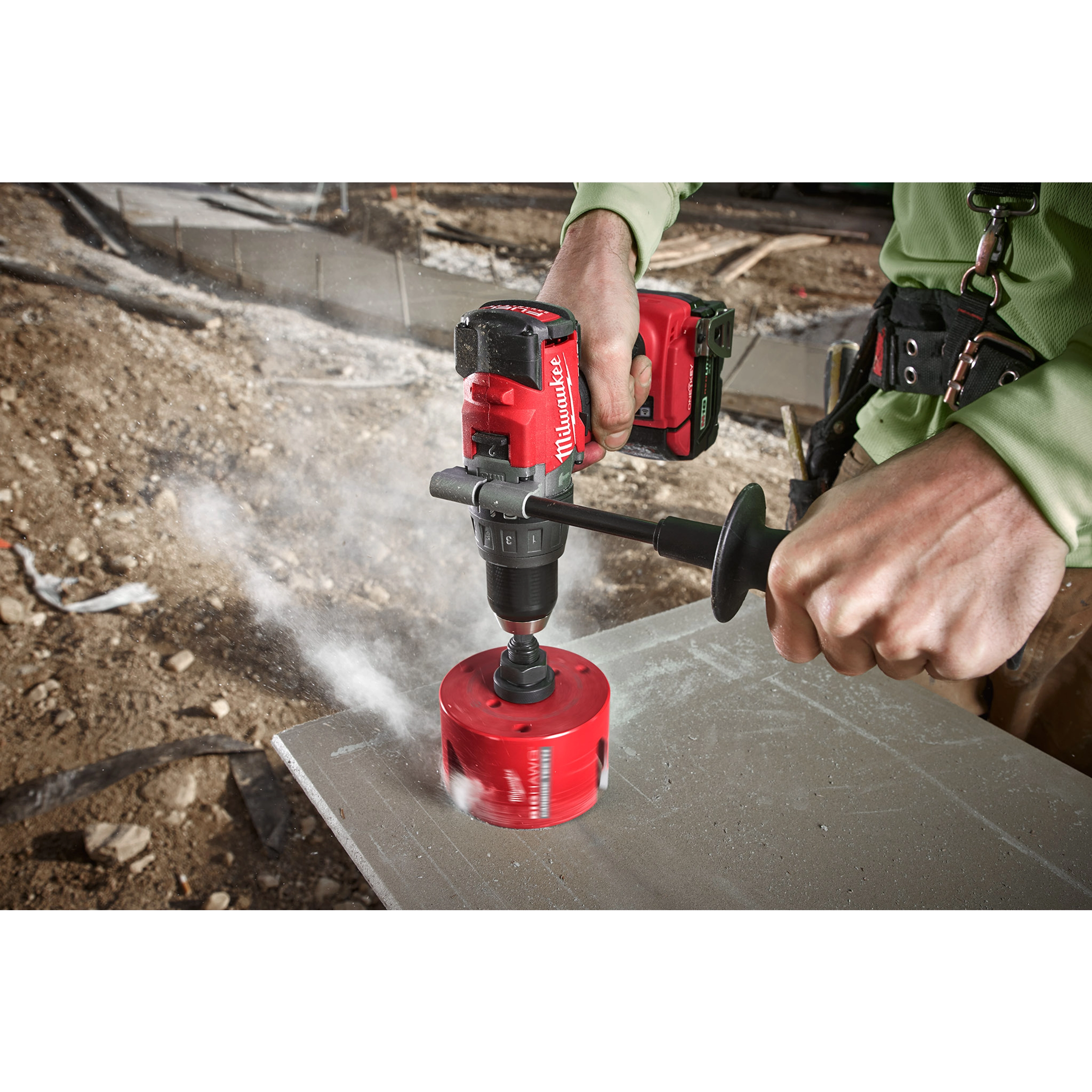 Person using a red cordless drill with 4-1/4" BIG HAWG with Carbide Teeth to drill through a concrete surface at a construction site.
