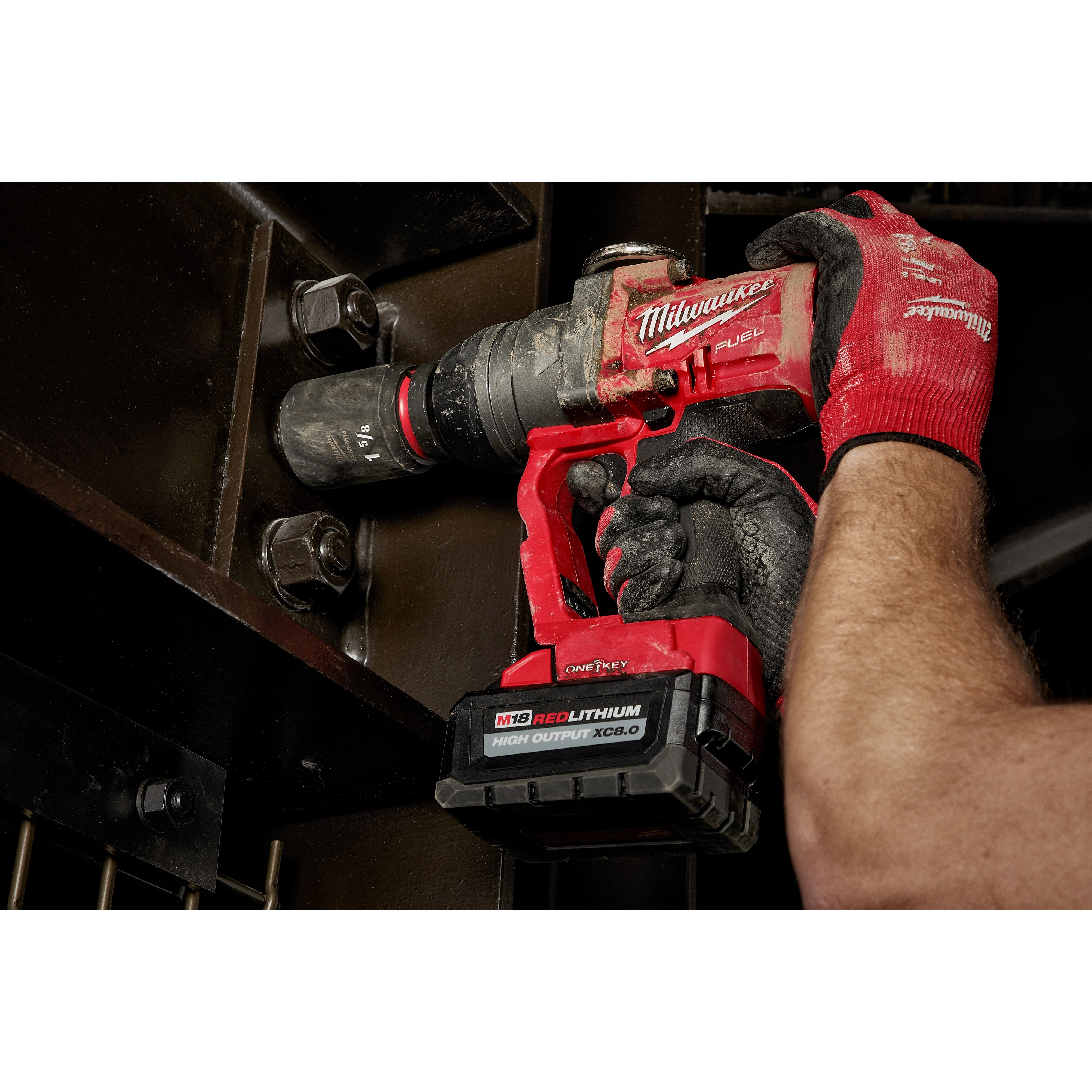 A person uses the SHOCKWAVE™ Impact Duty™ 1’’ Drive 1-5/8’’ Deep 6 Point Socket with a red power tool to tighten bolts on a metal structure. The person's hands are wearing red and black gloves.
