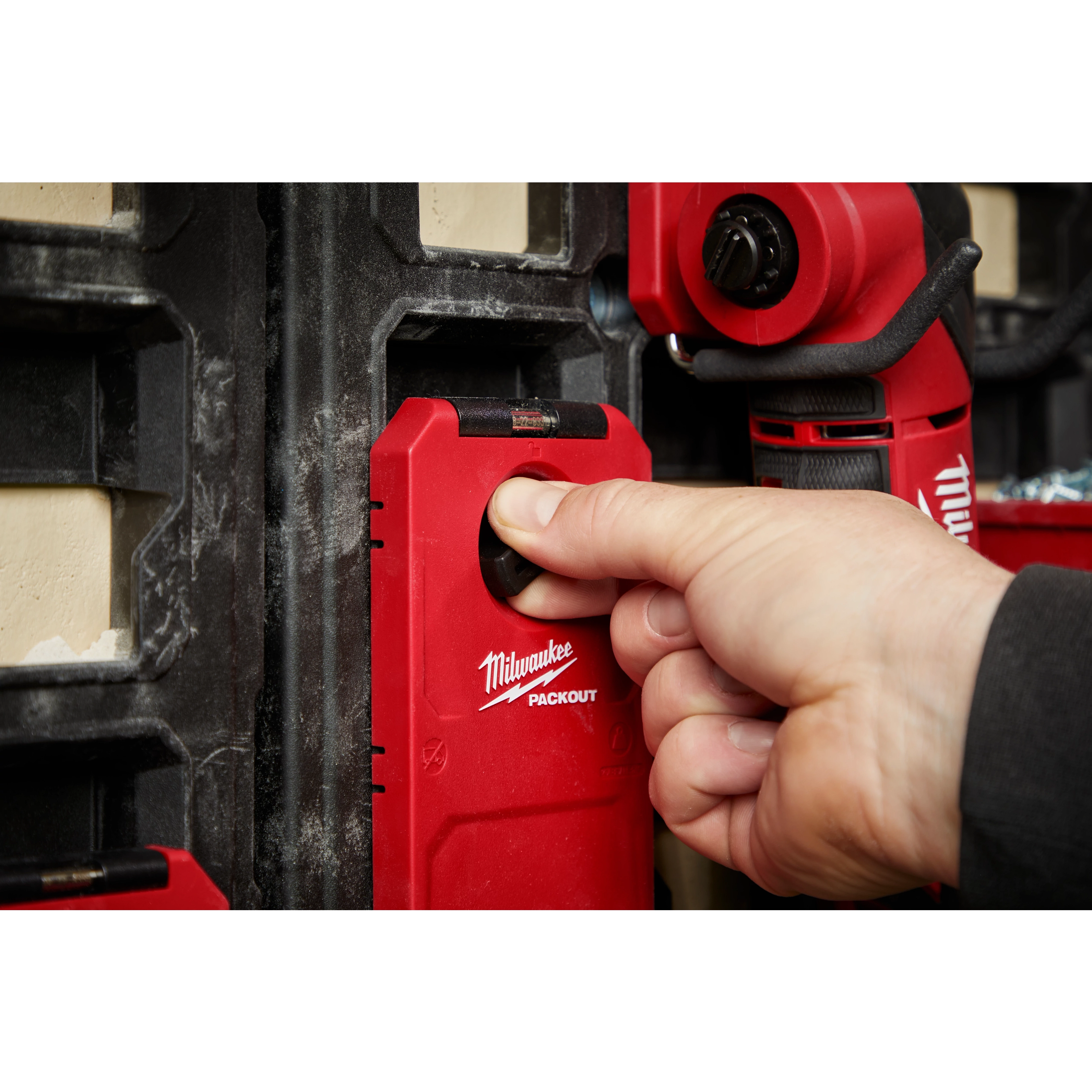A hand is adjusting the twist dial on the PACKOUT™ Shop Storage Twist Dial Close Up. The red product is mounted on a black wall panel system, featuring prominently a twist-lock mechanism for secure storage.