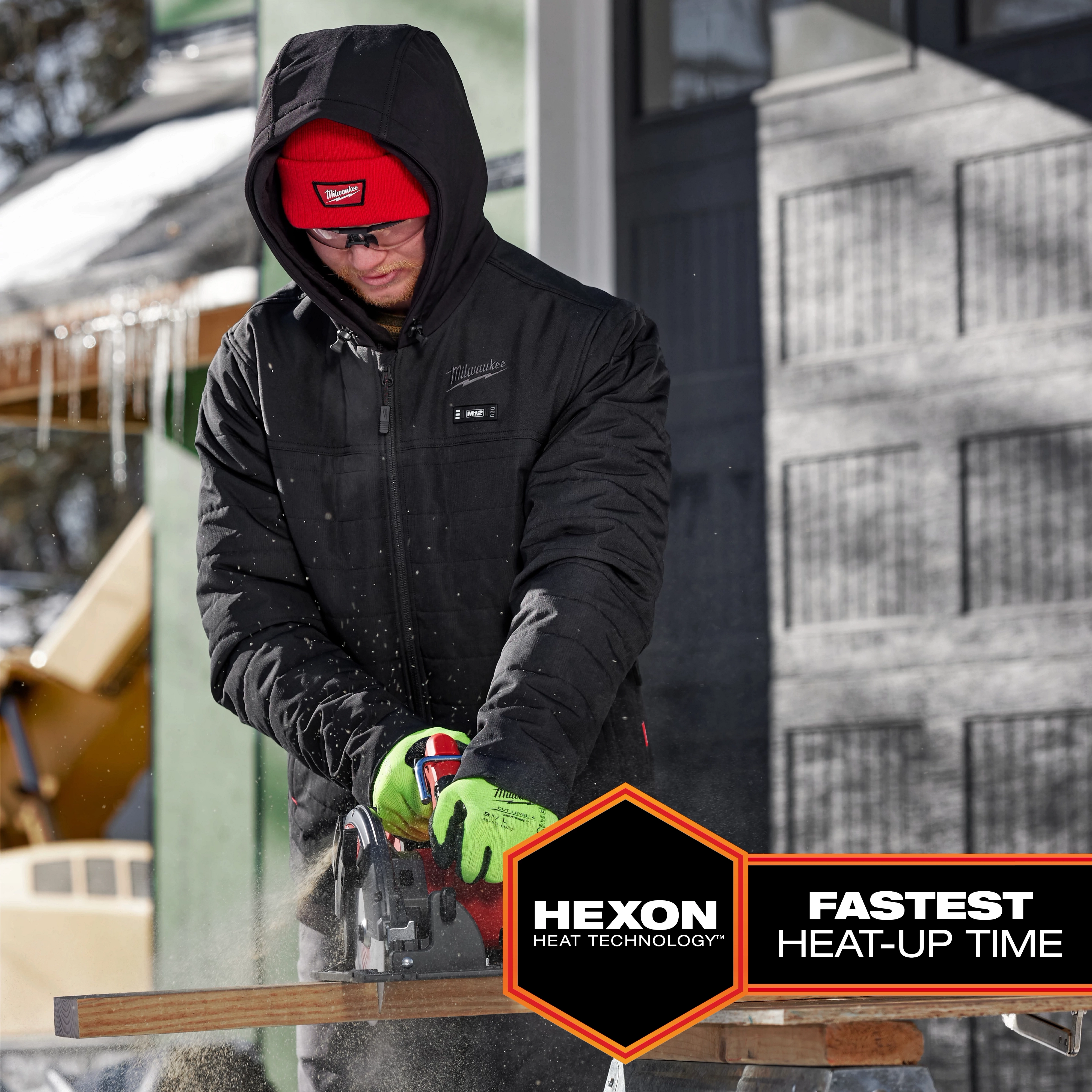 Person using a power saw outdoors while wearing a black M12 Heated AXIS Jacket with Hexon Heat Technology and text "Fastest Heat-Up Time" displayed.