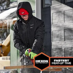 Person using a power saw outdoors while wearing a black M12 Heated AXIS Jacket with Hexon Heat Technology and text "Fastest Heat-Up Time" displayed.