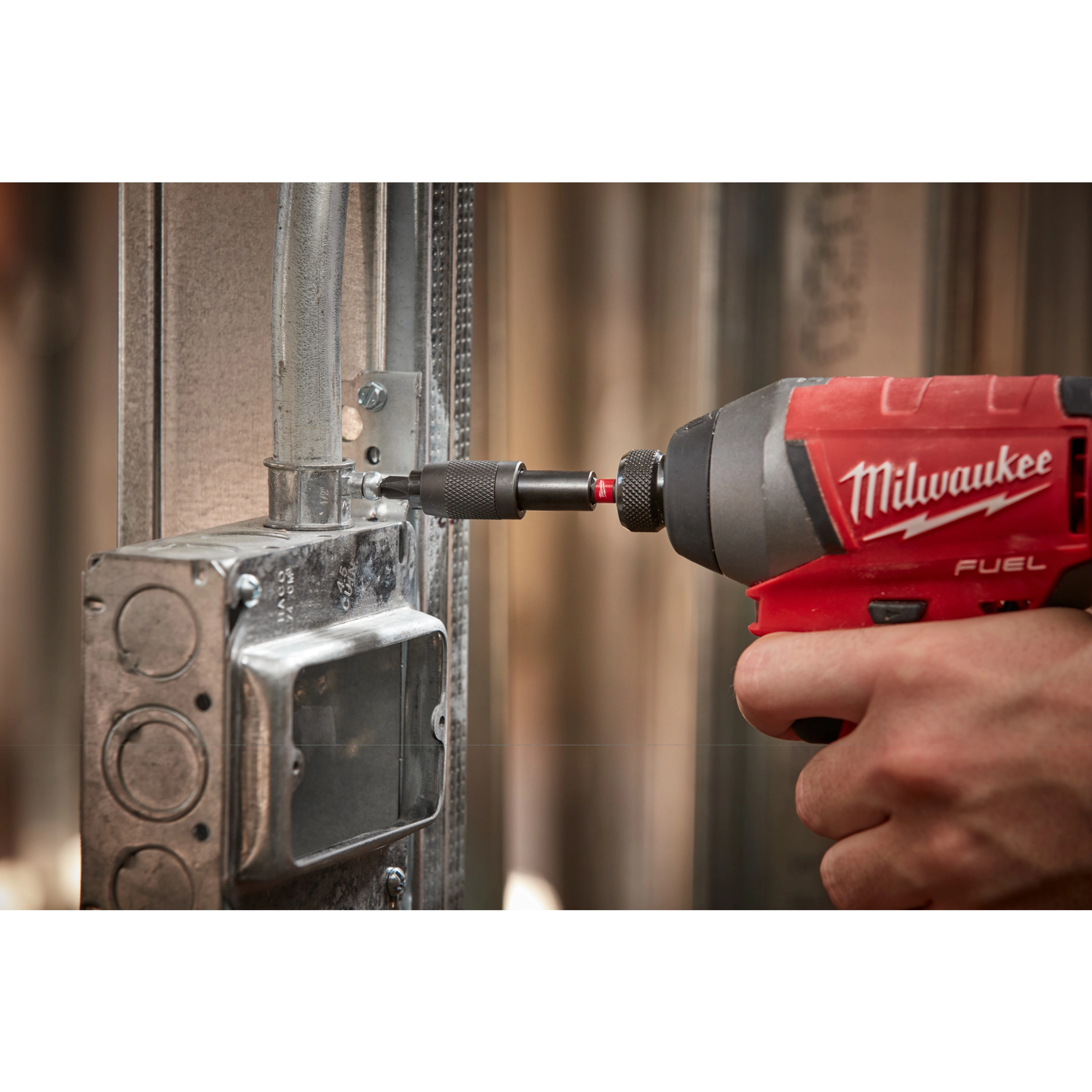 A person uses a Milwaukee drill with a SHOCKWAVE Impact Locking Bit Holder to fasten a screw into a metal electrical box.