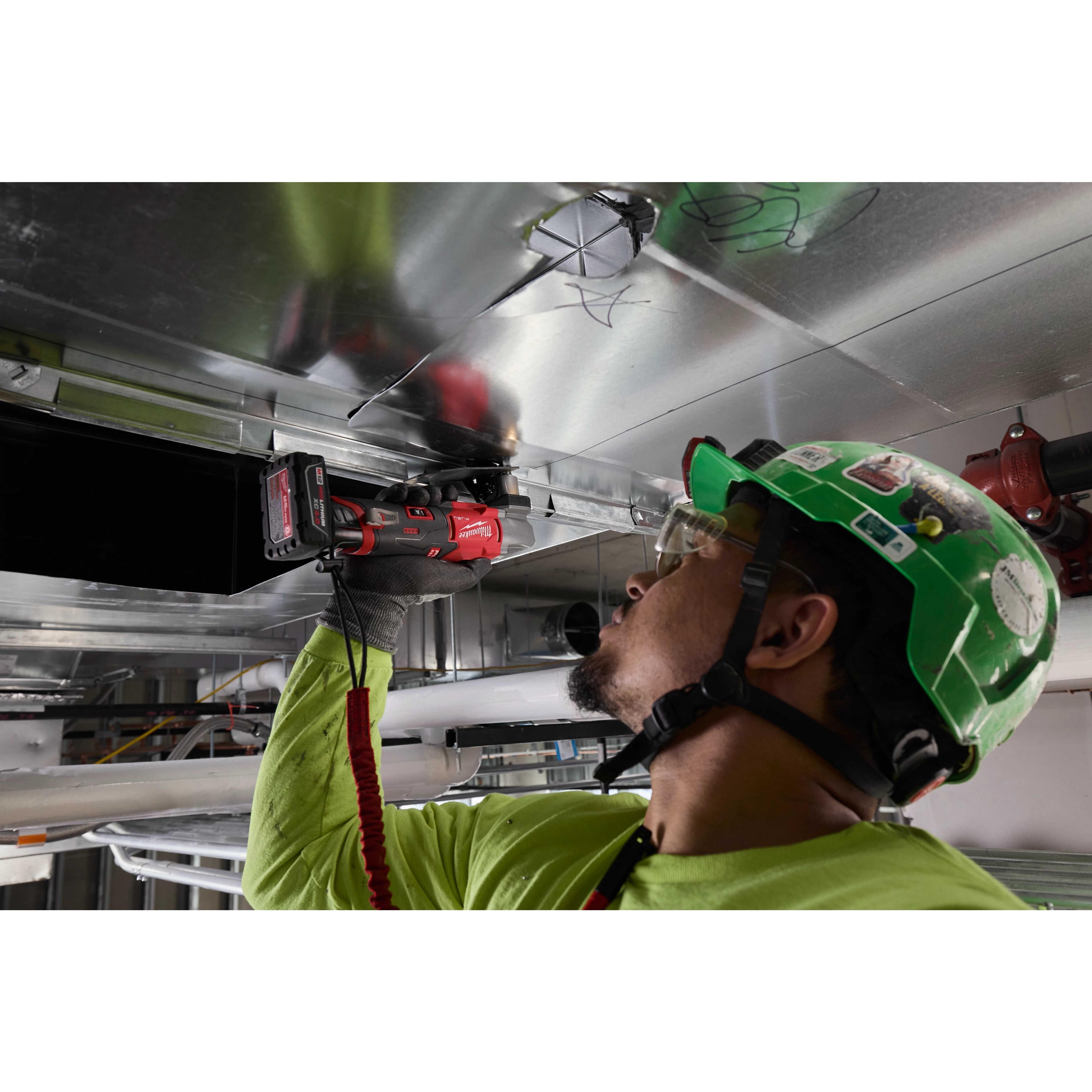 Worker using an M12 FUEL 16 Gauge Scroll Shear to cut overhead metal ducting.