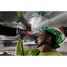 Worker using an M12 FUEL 16 Gauge Scroll Shear to cut overhead metal ducting.