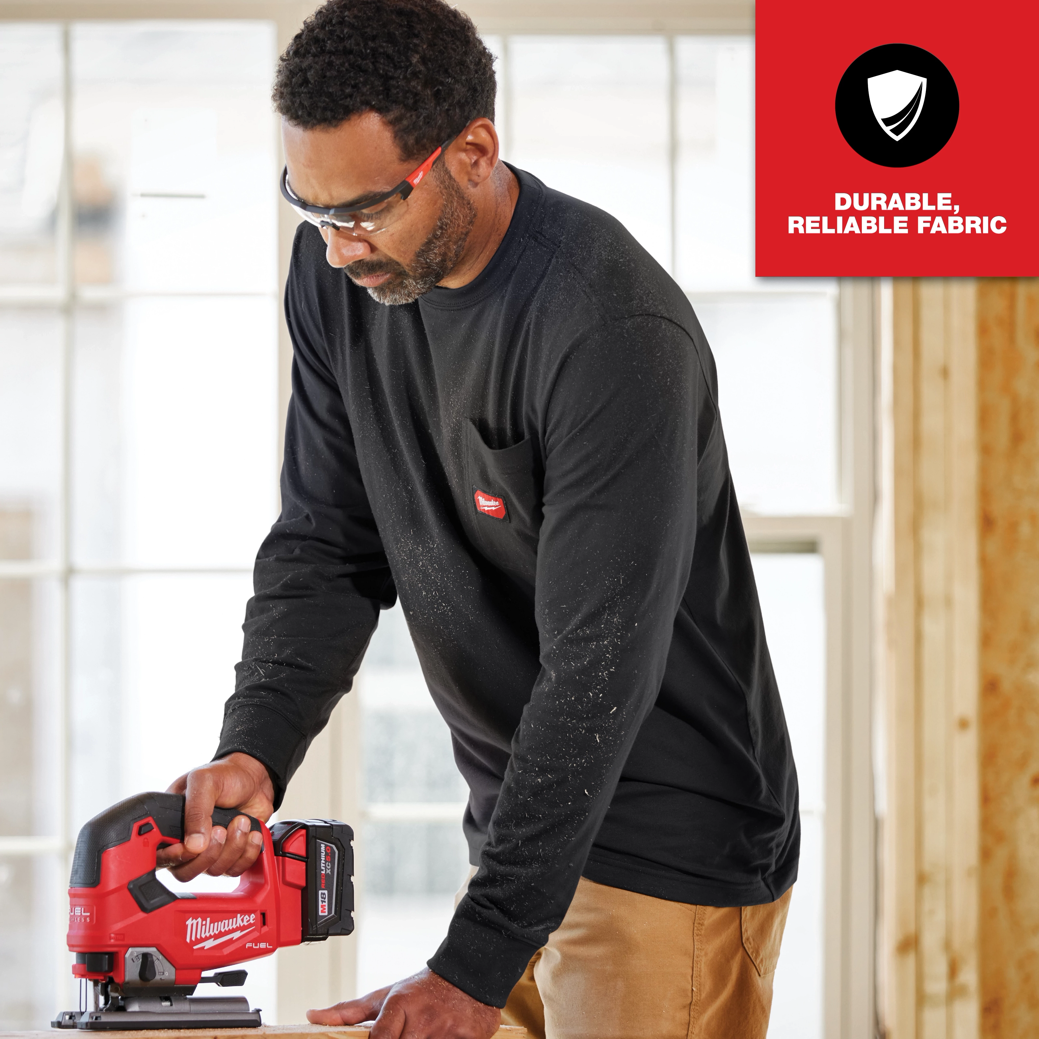 A person wearing a GRIDIRON Pocket T-Shirt - Long Sleeve, holding a red and black power tool, with "Durable, Reliable Fabric" text.
