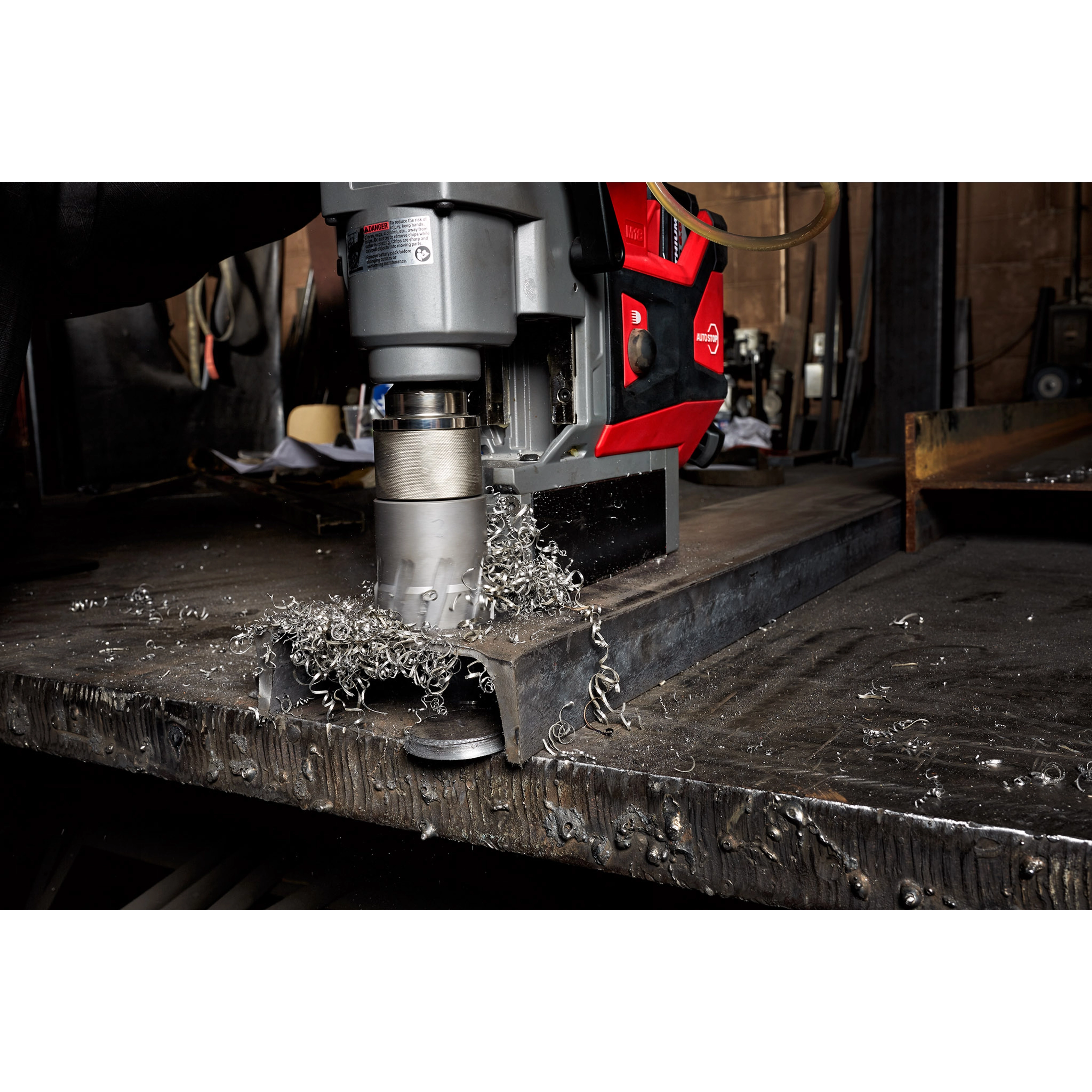 Annular Cutter attached to a red and gray power drill, drilling into metal with metal shavings scattered on the surface.