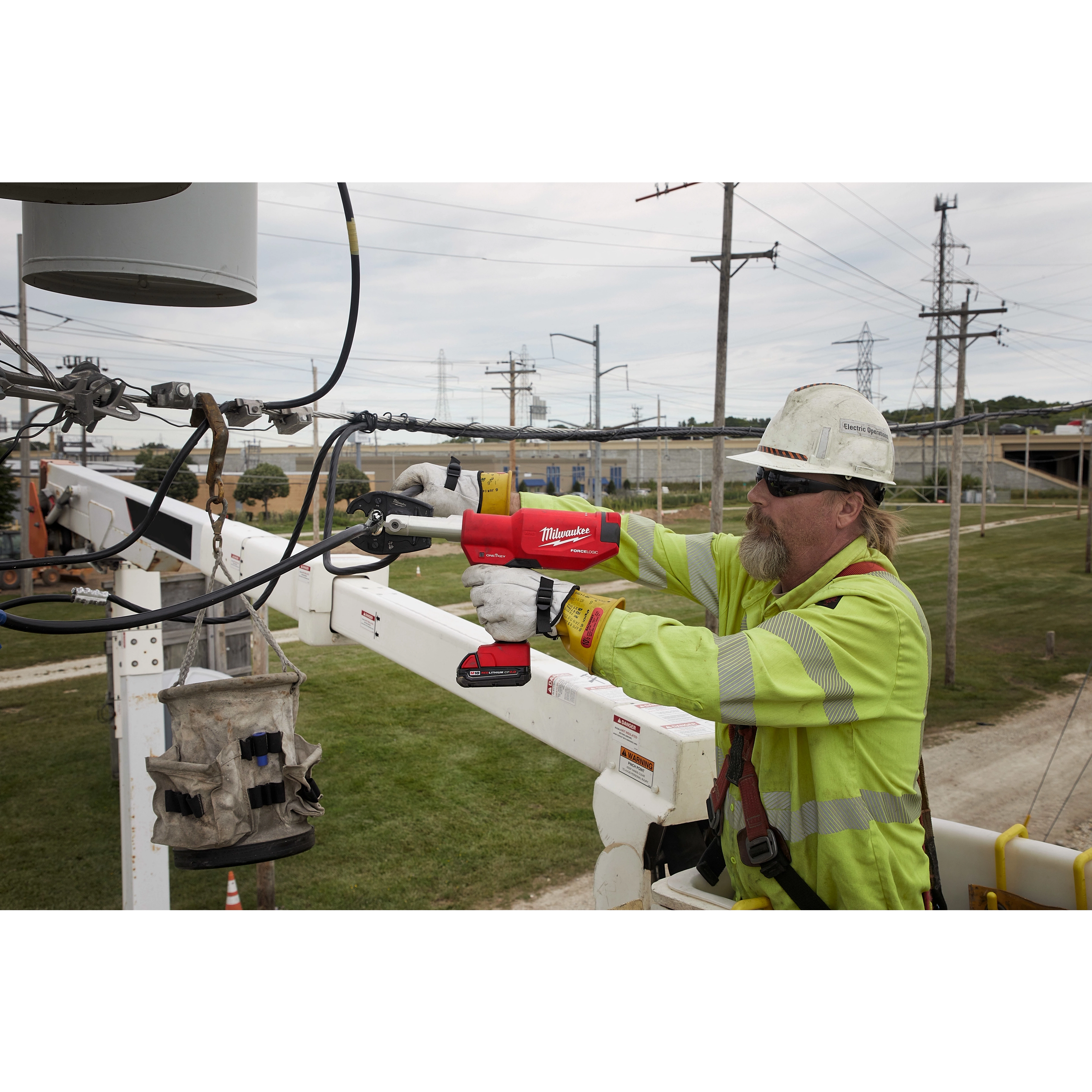 A utility worker uses an M18 FORCE LOGIC 6 Ton Pistol Utility Crimper to secure a connection on overhead power lines from a bucket truck.