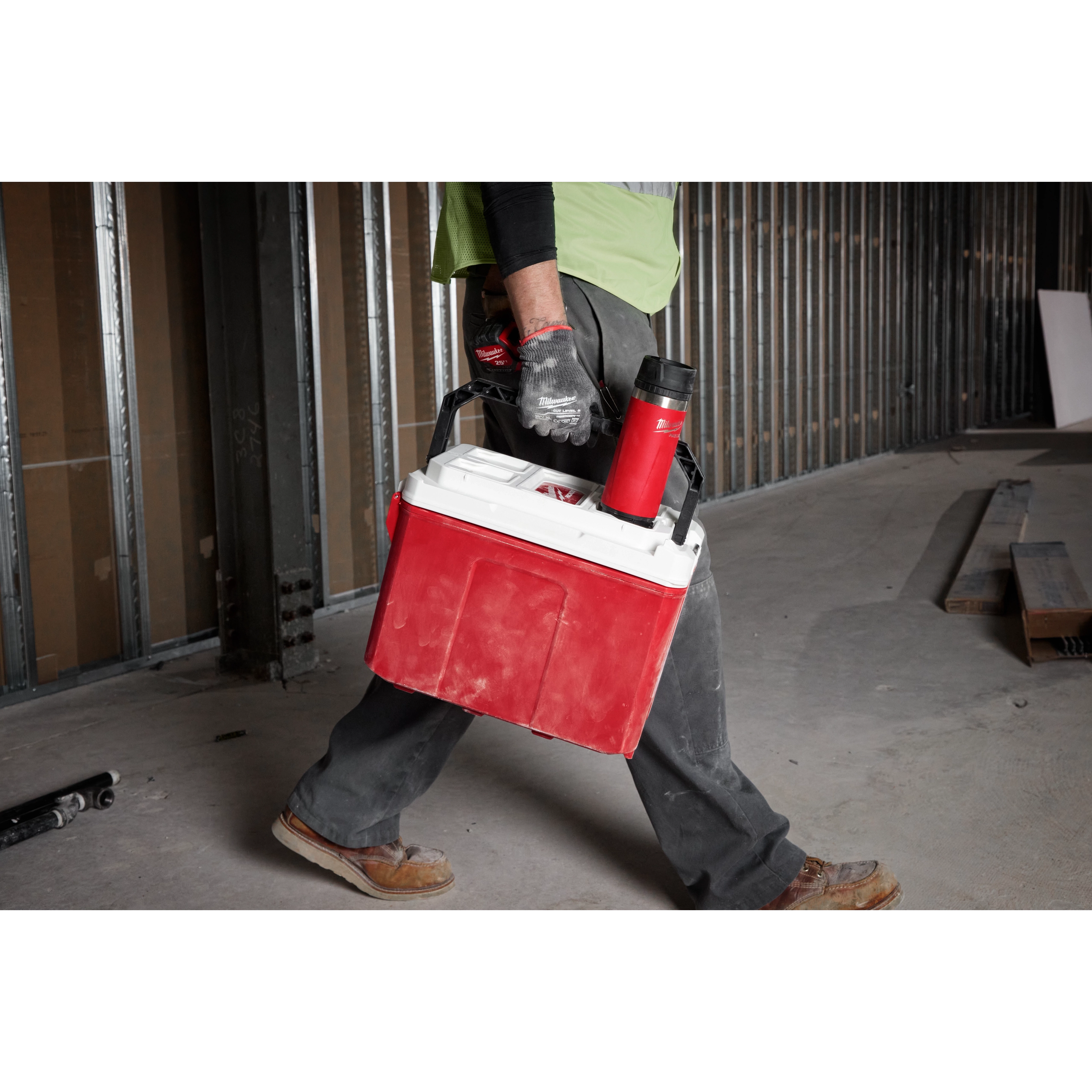 Worker carrying a red cooler in a construction site with a red PACKOUT 18oz Insulated Bottle with Sip Lid attached to it.