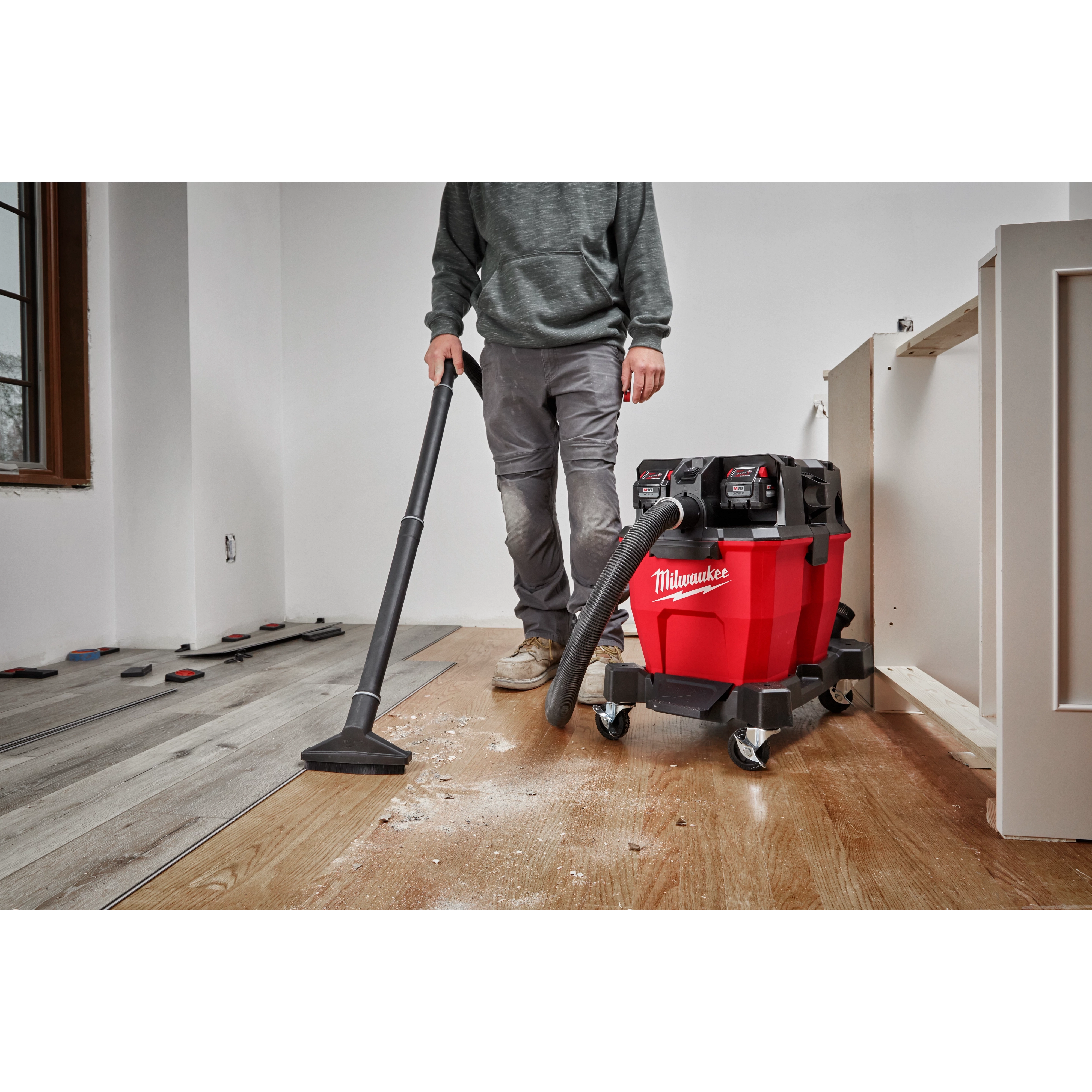 Person using the Milwaukee M18 FUEL 9 Gallon Dual-Battery Wet/Dry Vacuum to clean up wood debris on a wooden floor in a room.