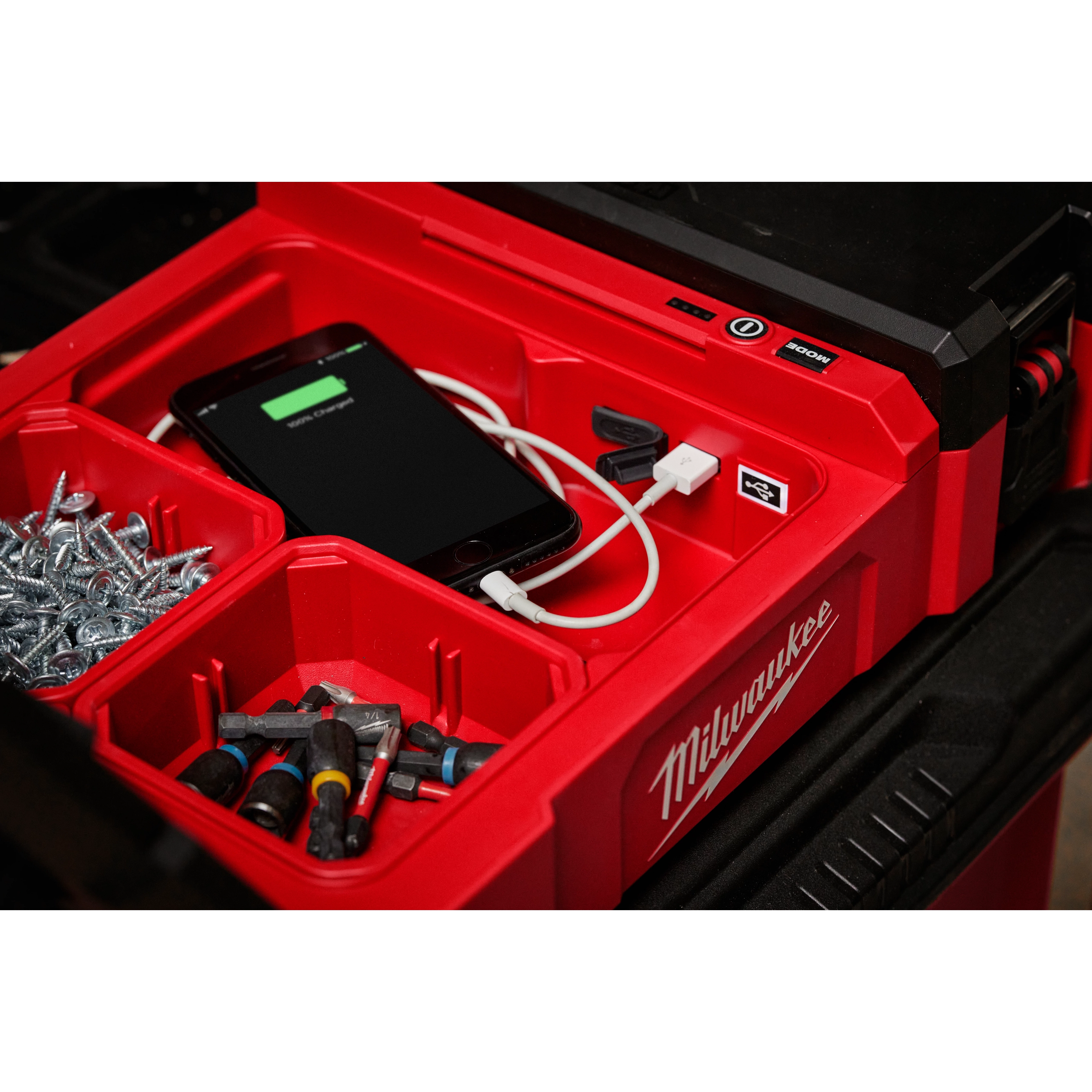 M12 PACKOUT Flood Light with USB Charging shown with various tools, screws, and a phone being charged inside a red tool organizer.