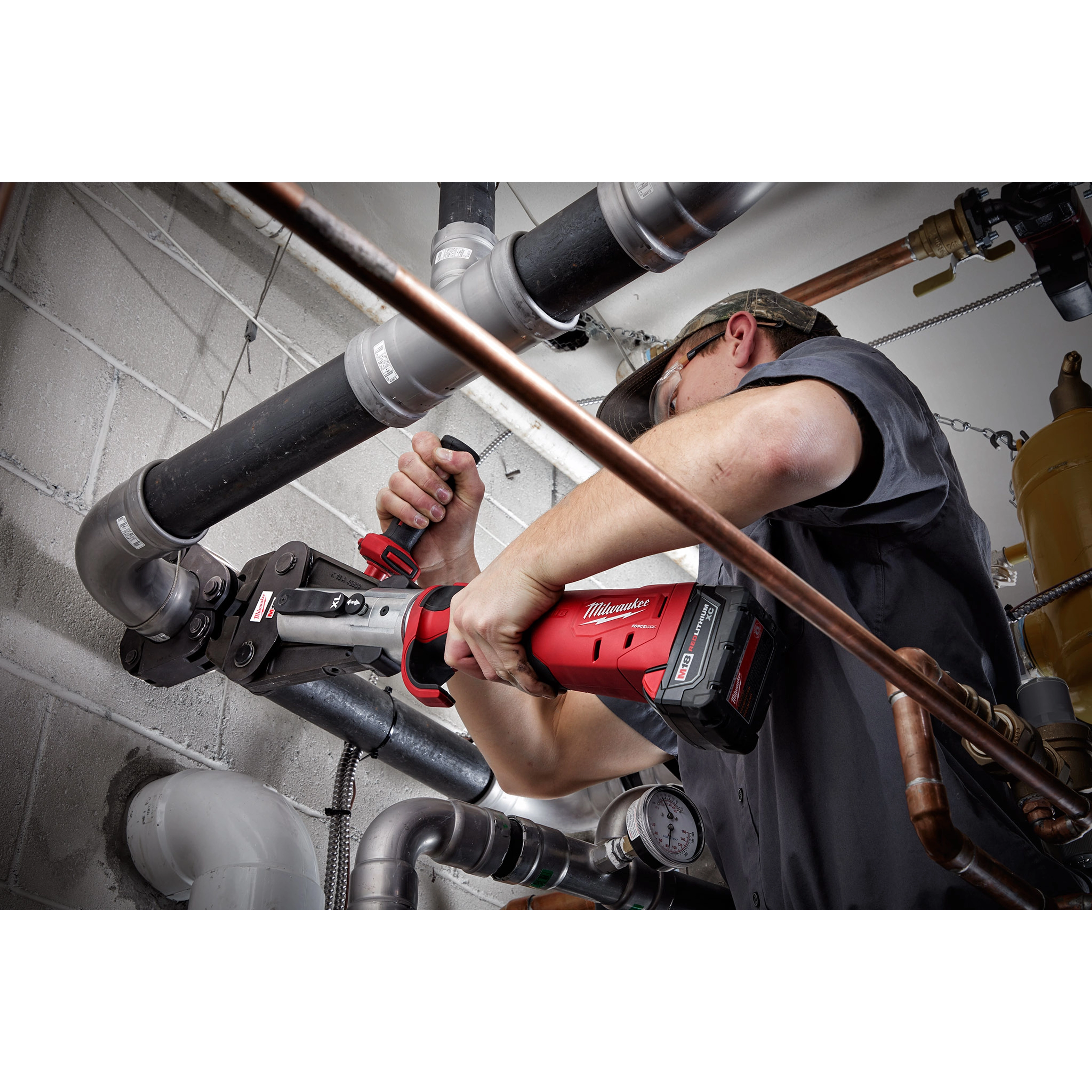 Worker using 2½” - 4” IPS XL Ring Kit for M18 FORCE LOGIC Long Throw Press Tool on black pipes in an industrial setting.