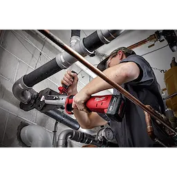 Worker using 2½” - 4” IPS XL Ring Kit for M18 FORCE LOGIC Long Throw Press Tool on black pipes in an industrial setting.